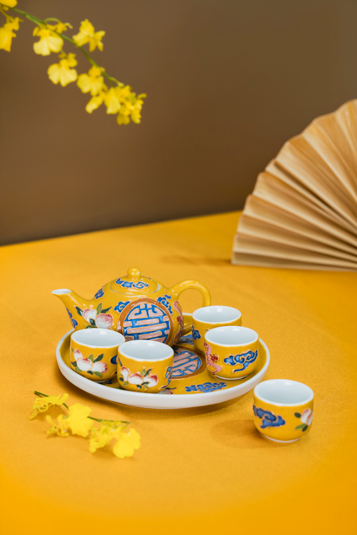 Free Bright yellow ceramic tea set with floral pattern on a yellow surface and brown backdrop. Stock Photo