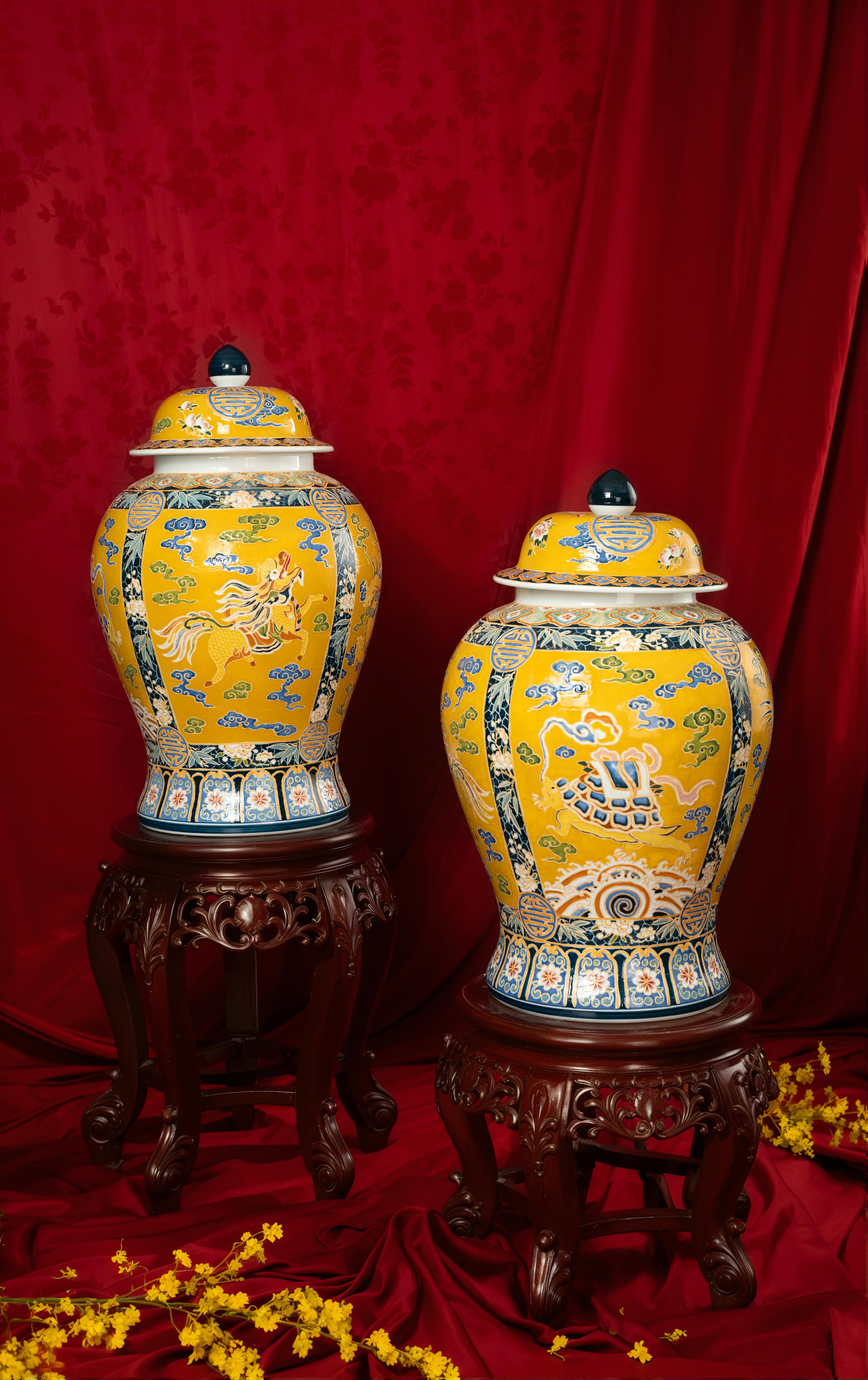 grátis Vasos ornamentados amarelos com padrões de dragão sobre suportes de madeira esculpida contra um fundo vermelho. Foto profissional