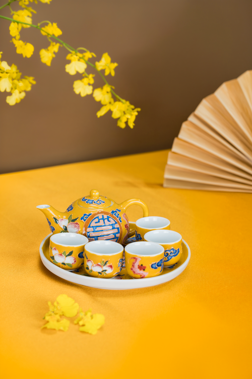 Free Yellow ceramic tea set with floral designs on a matching tablecloth, adorned by origami fan. Stock Photo