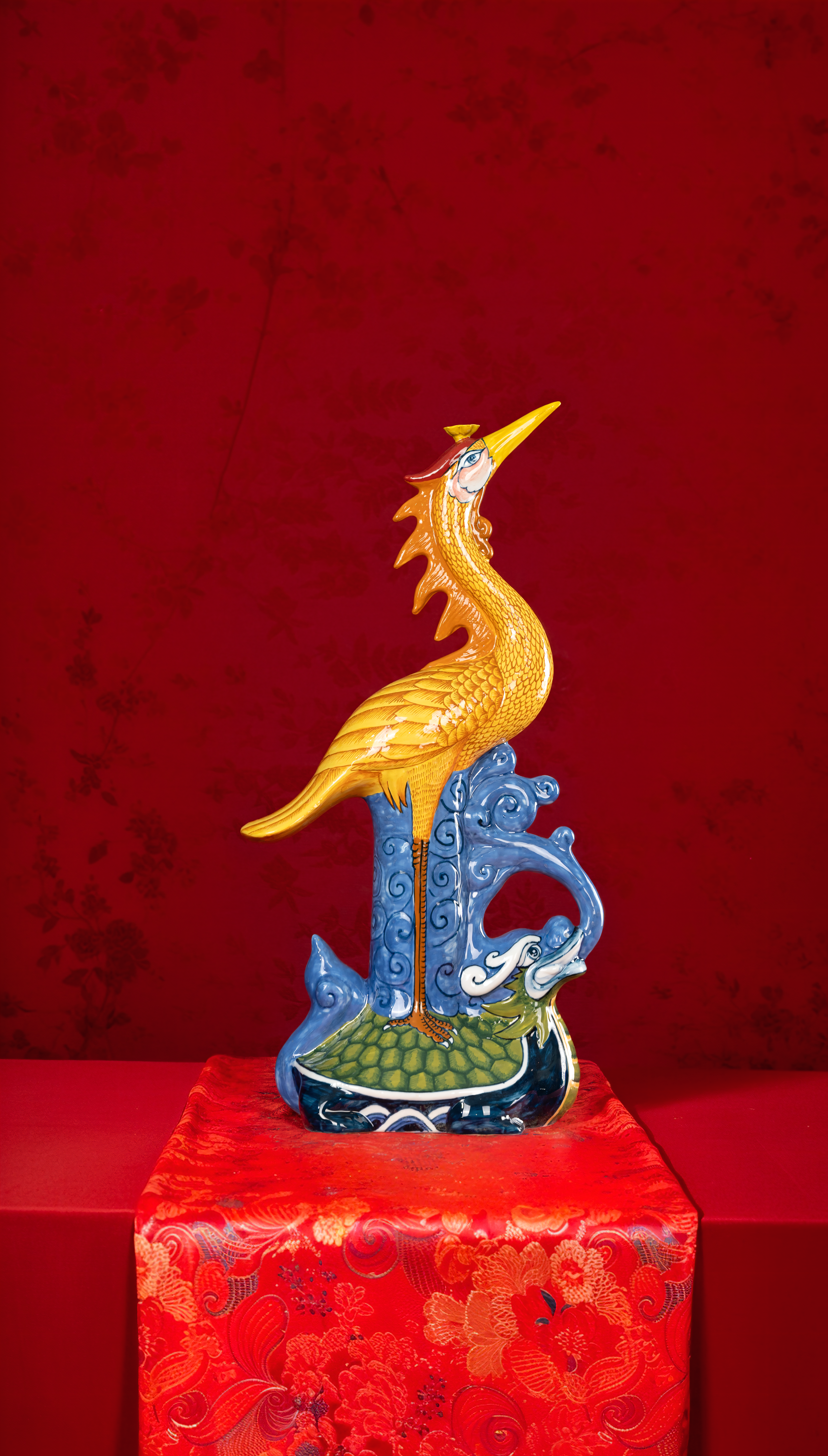 Vibrant decorative ceramic statue of a crane on a red ornate cloth.