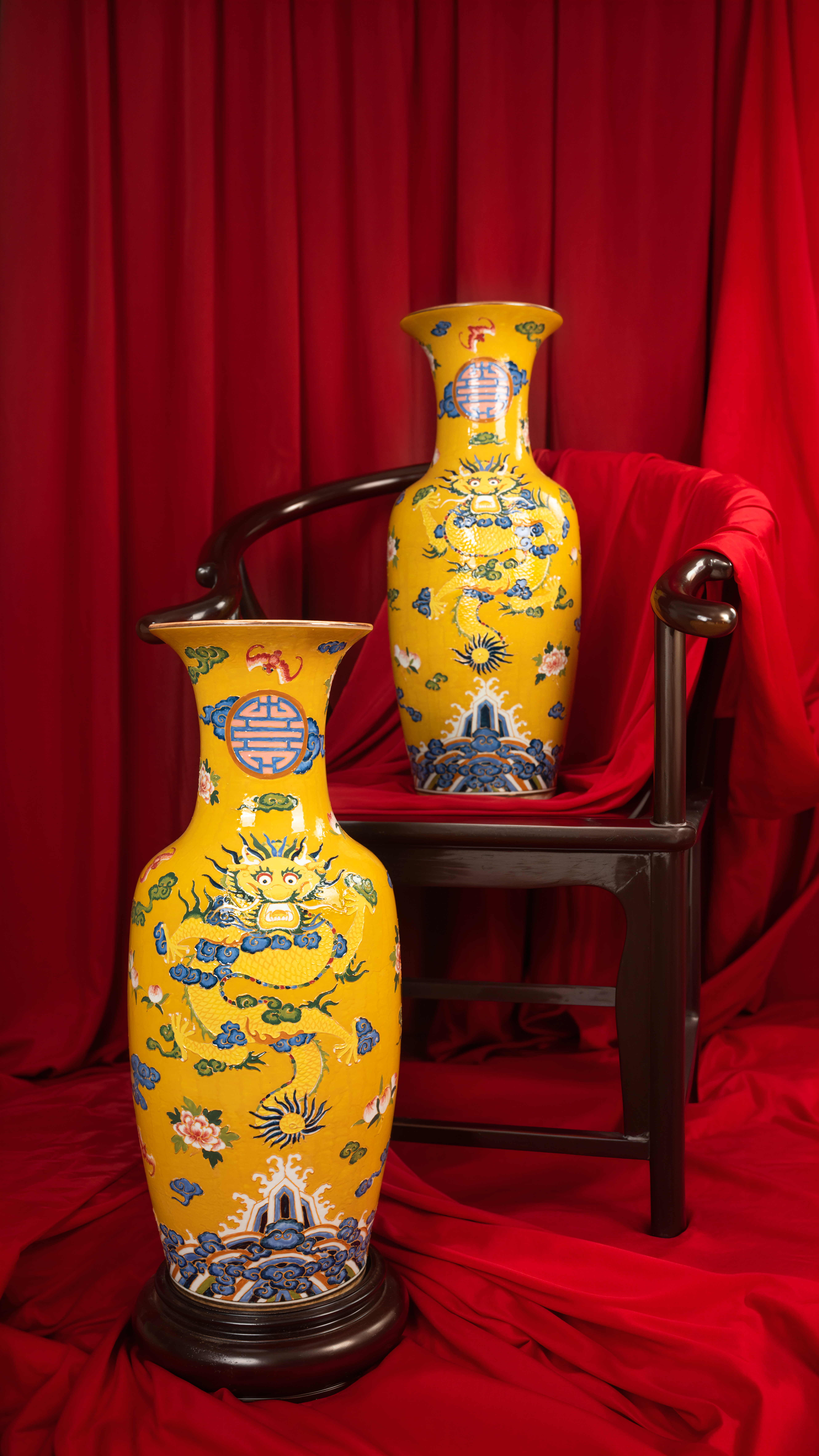 Two ornate yellow ceramic vases displayed against a rich red backdrop, showcasing intricate designs.