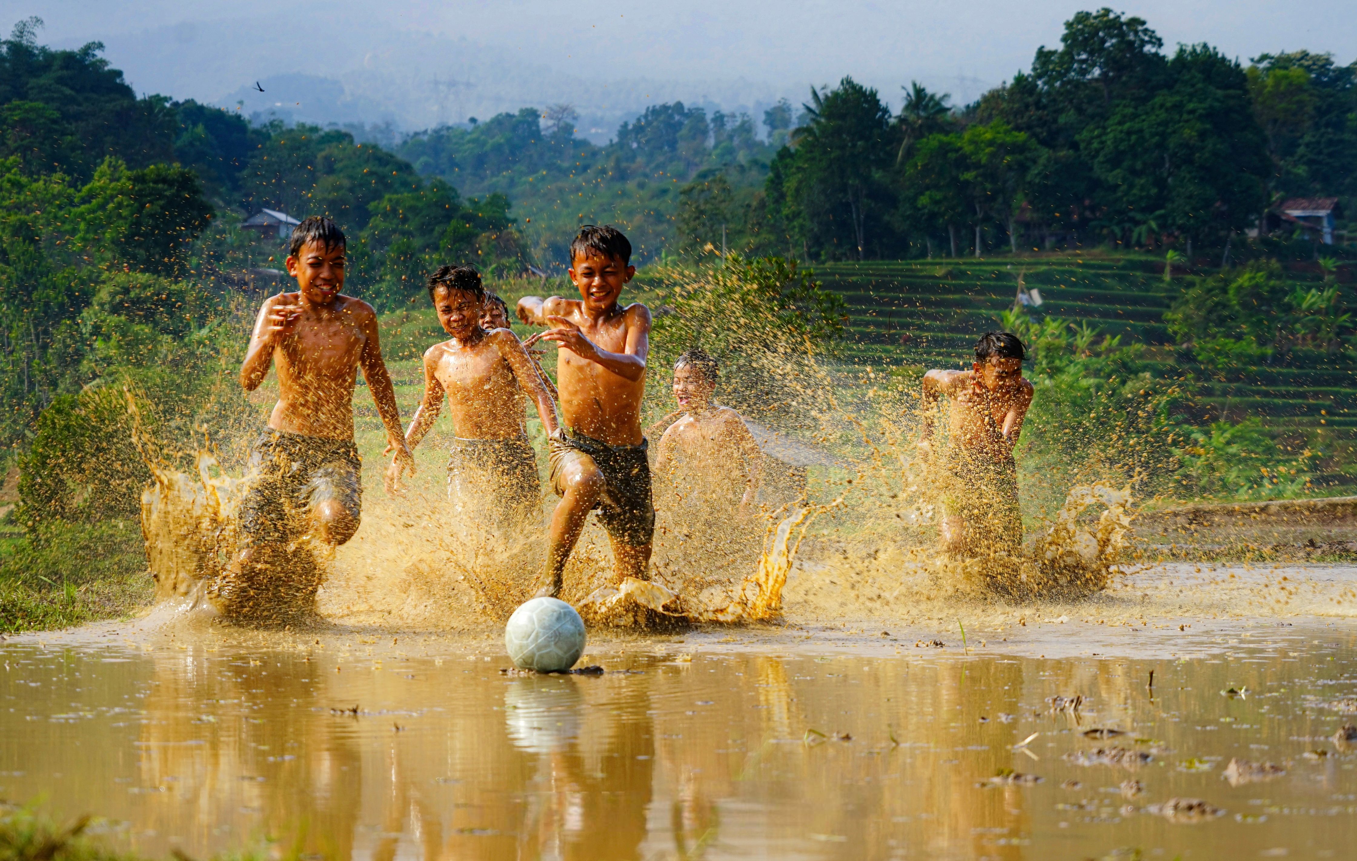 Children Playing with Soccer Ball in Muddy Rice Field