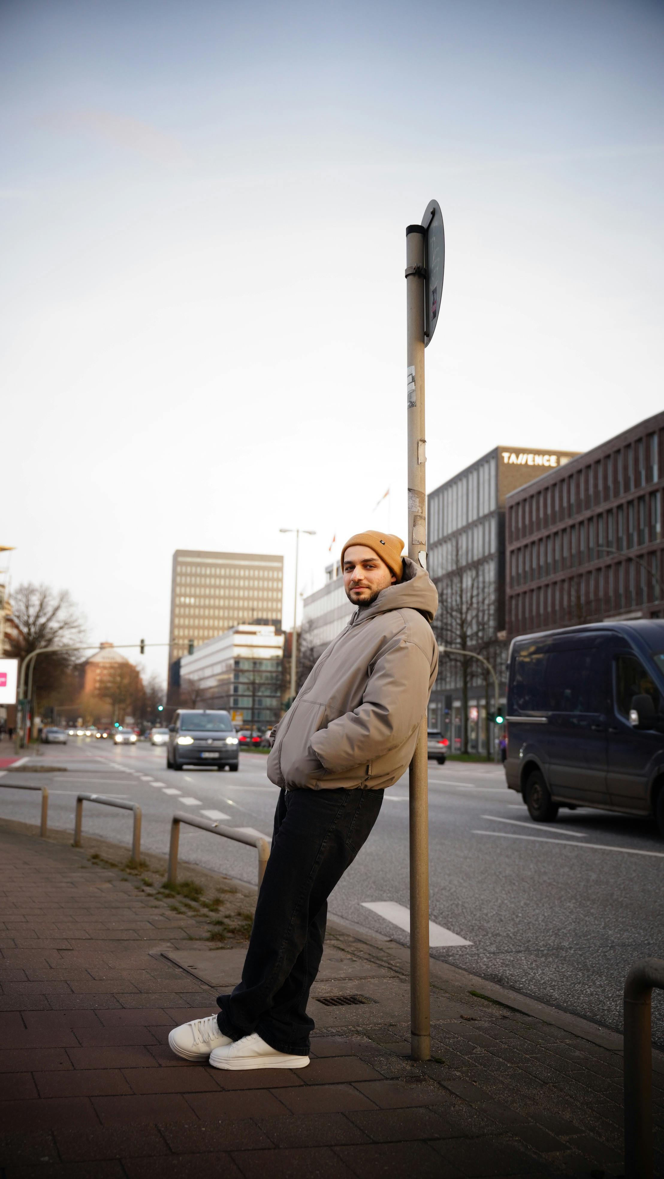 Casual young man in city street, wearing jacket and beanie, relaxing.