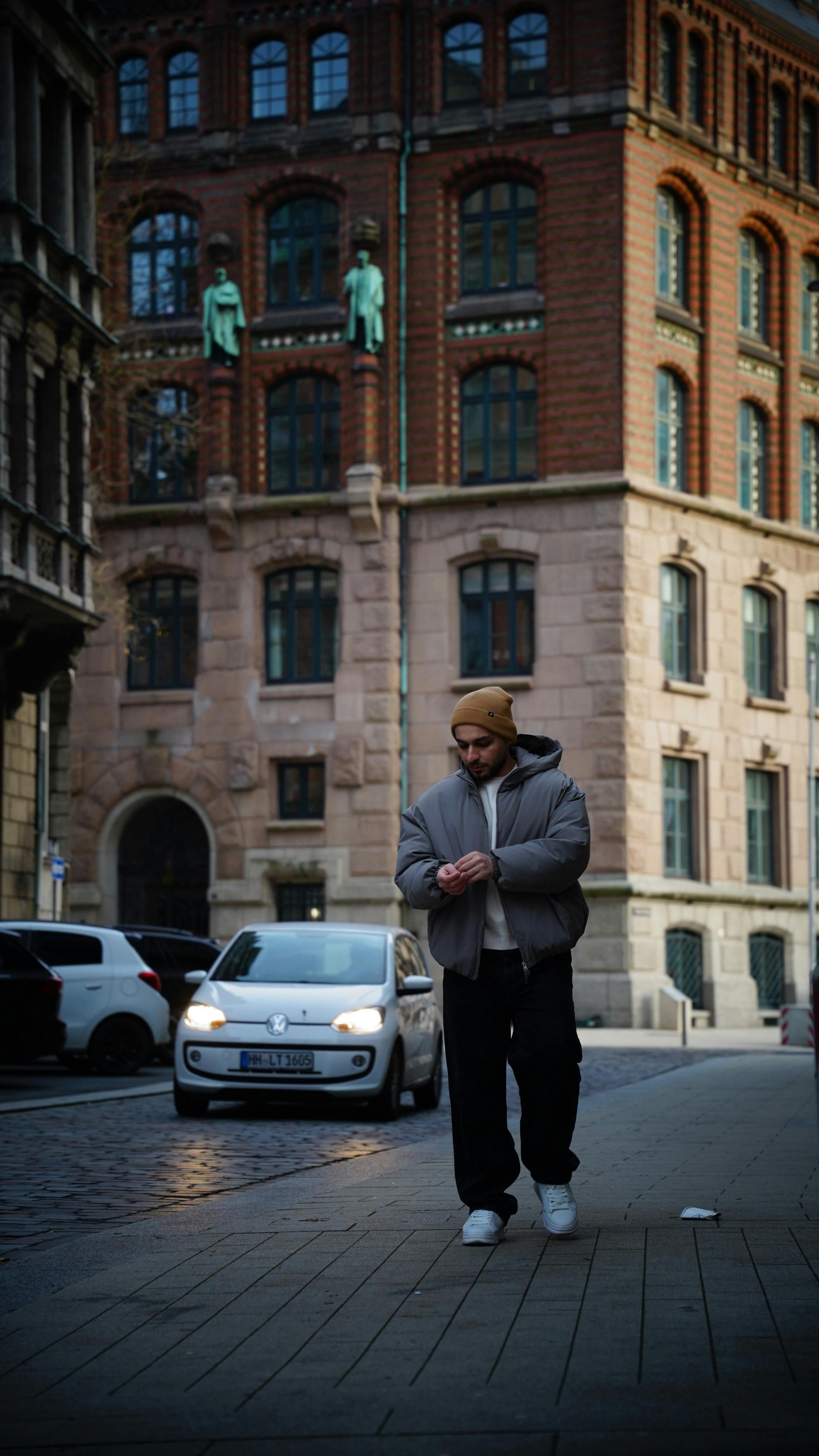 Kostnadsfria Man går på stadsgata bredvid en historisk byggnad med bilar som passerar på en lugn dag. Stock foto