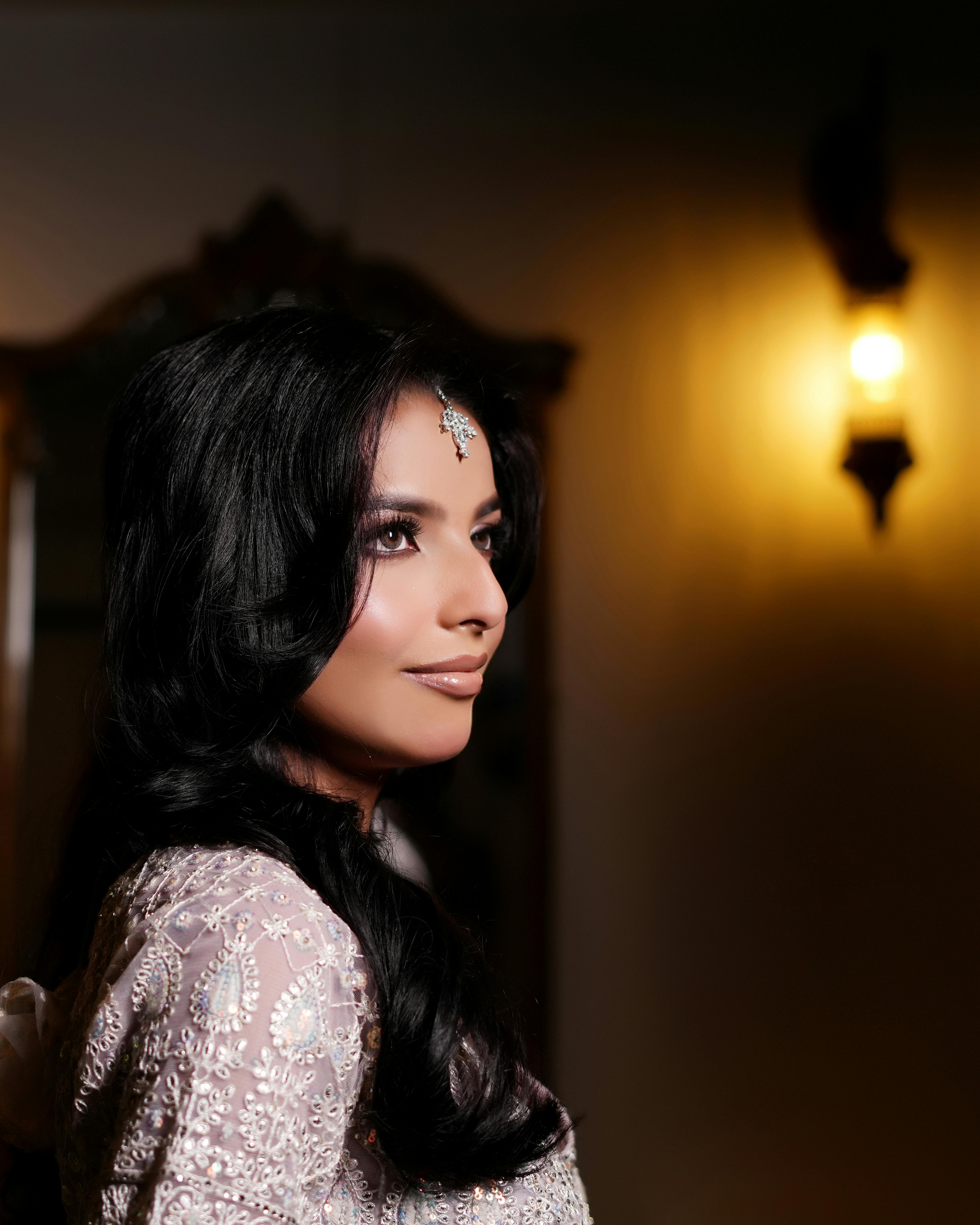 De franc Una bella dona vestida amb vestit tradicional posa amb gràcia a l'interior, il·luminada per una il·luminació càlida. Foto d'estoc