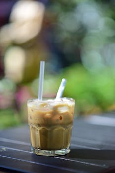 A glass of iced coffee with two straws on a table set outdoors, perfect for a summer refreshment.