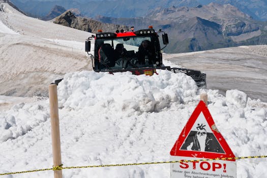 Snowplow clearing snow in the Swiss Alps with stop sign in foreground.