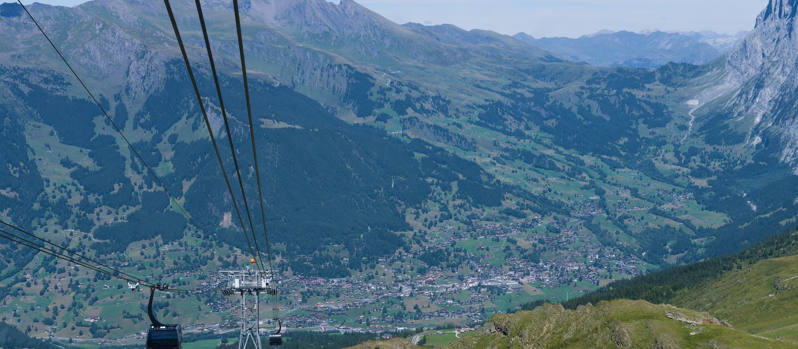 Breathtaking aerial view of Grindelwald and Swiss Alps from a cable car, showcasing lush valleys and rugged peaks.