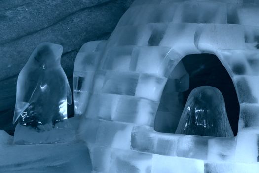 Intricate ice igloo sculpture featuring penguin figurines in an icy environment.