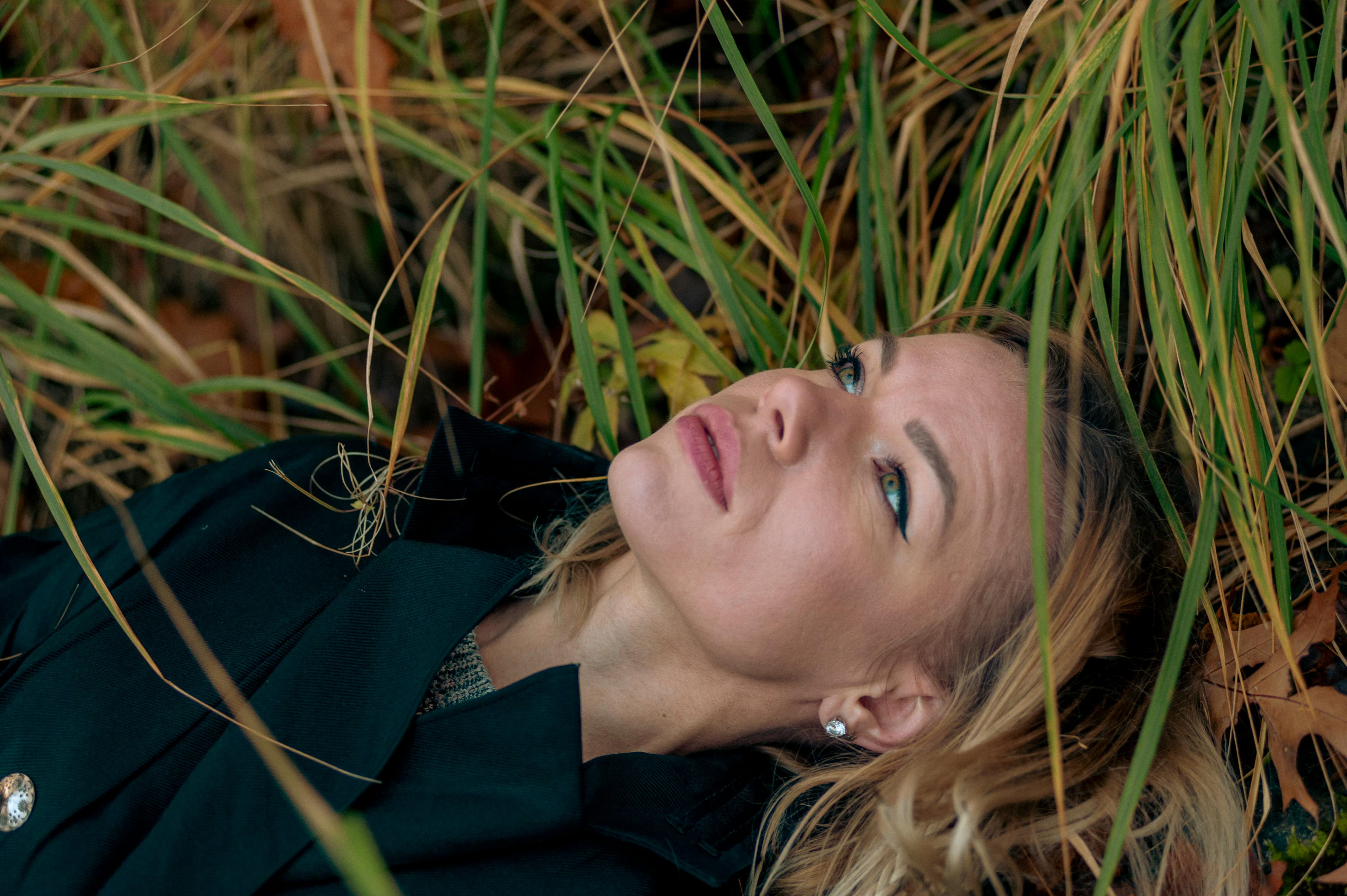 Kostenlos Eine nachdenkliche Frau liegt im Gras zwischen Herbstlaub und blickt gedankenverloren in die Ferne. Szene im Freien. Stock-Foto