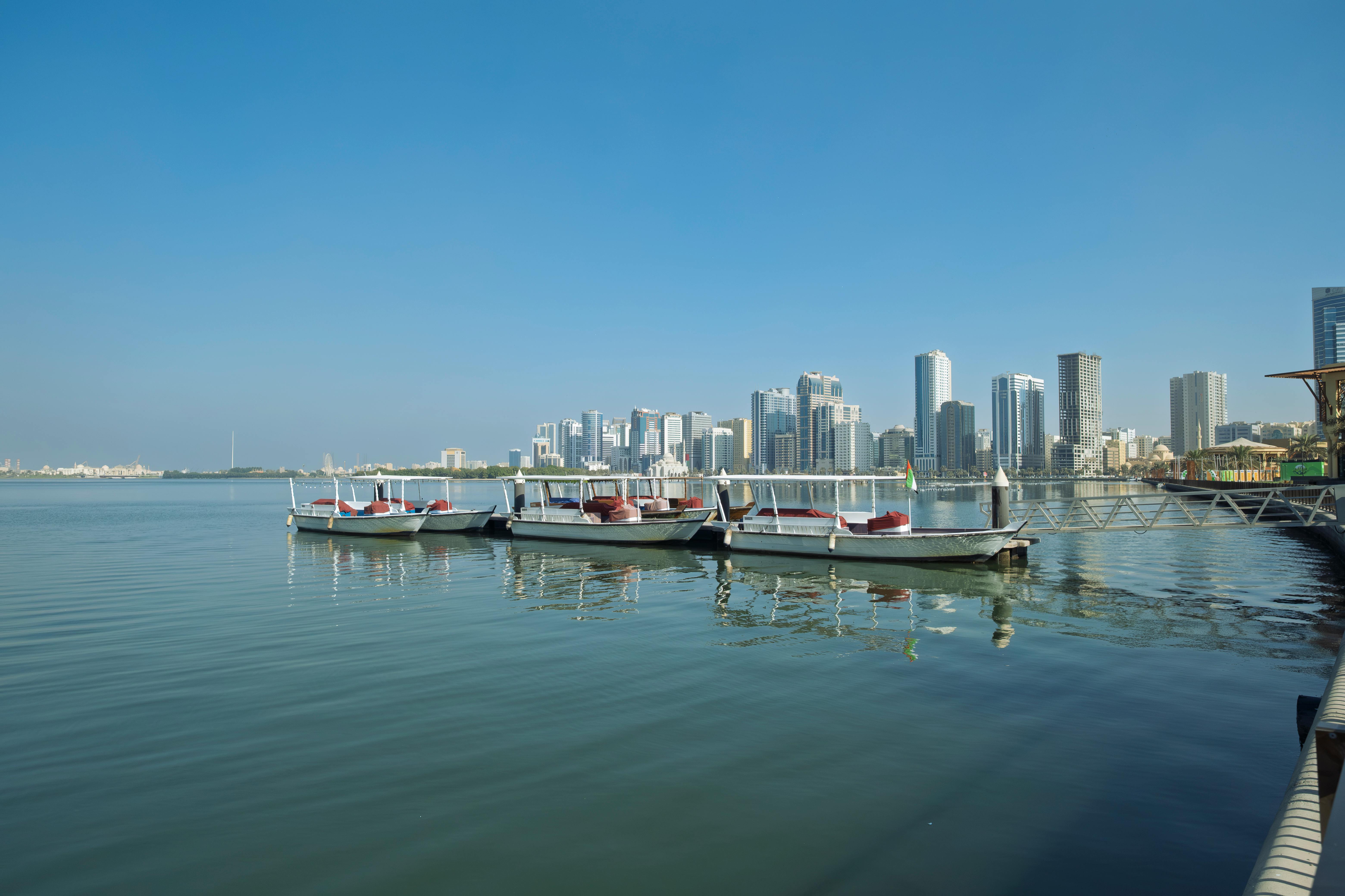 Tranquil boats on Sharjah's waterfront with impressive skyline and blue sky backdrop.