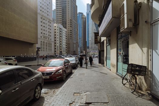 A lively street scene in Sharjah, UAE with bustling pedestrians and cars against a backdrop of skyscrapers.