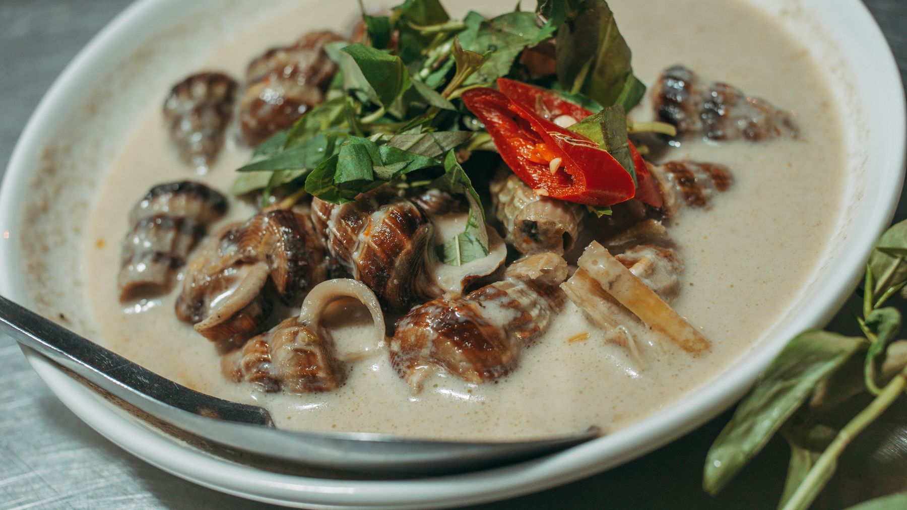 Bát canh hải sản đậm đà với ốc, rau thơm và nước cốt dừa.