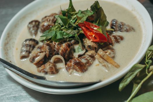 Flavorful seafood soup with snails, fresh herbs, and coconut milk in a white bowl.