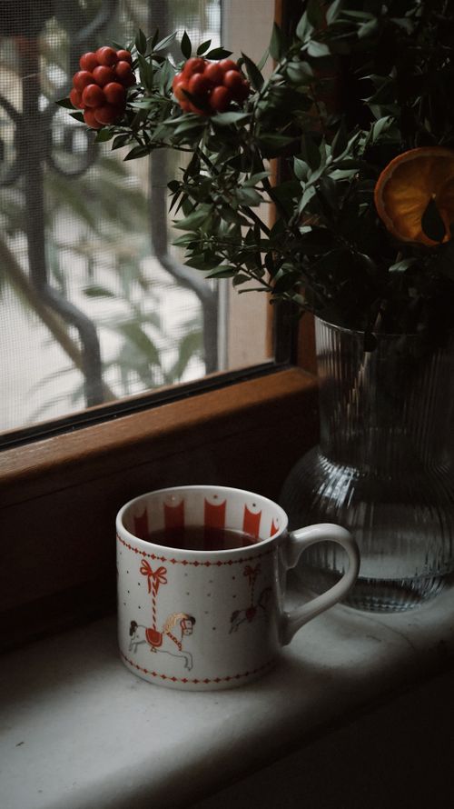 Free Festive coffee mug and vase by a window, evoking a cozy winter atmosphere. Stock Photo