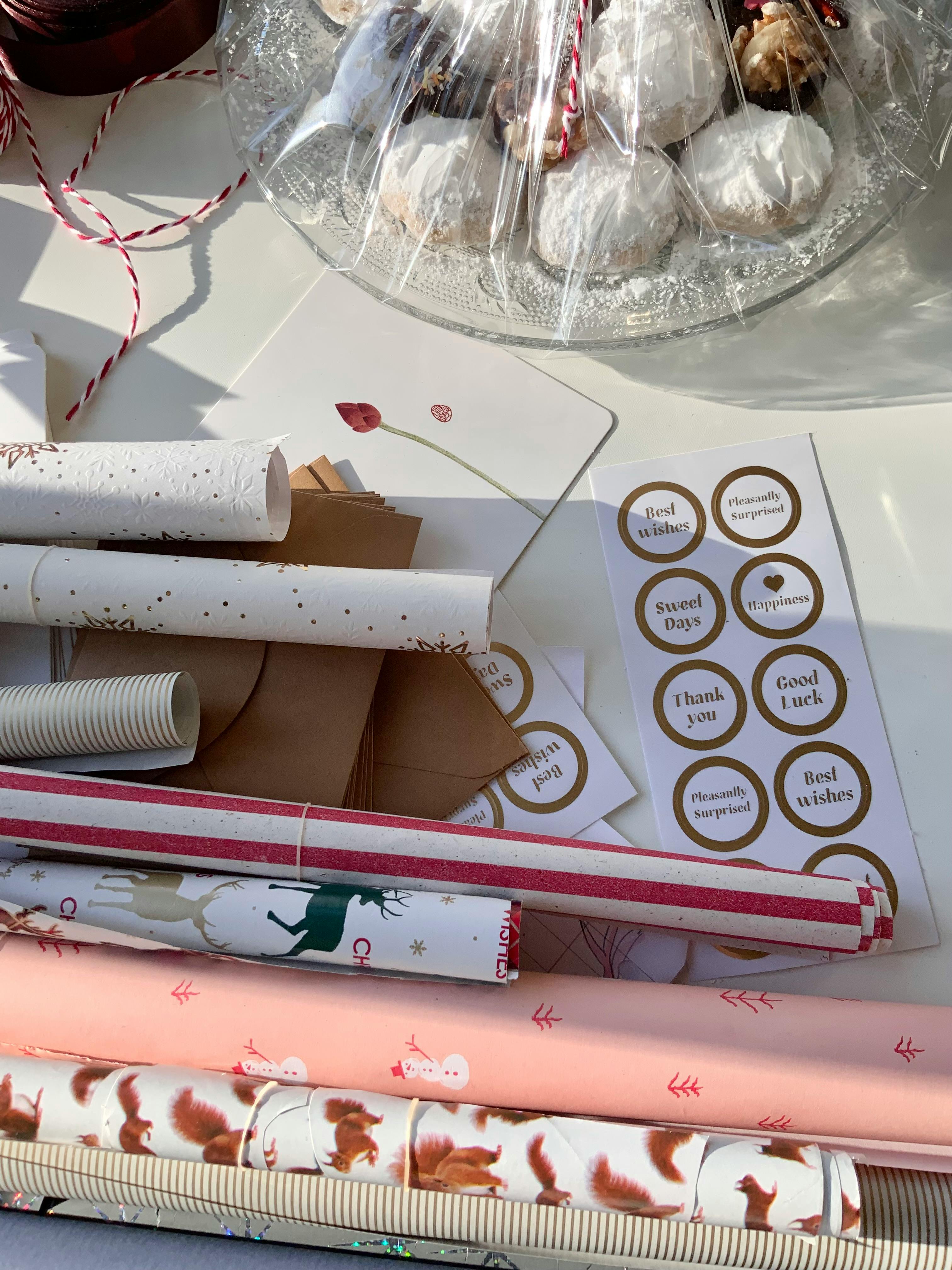 A collection of gift wrapping supplies with festive designs alongside a plate of wrapped treats.