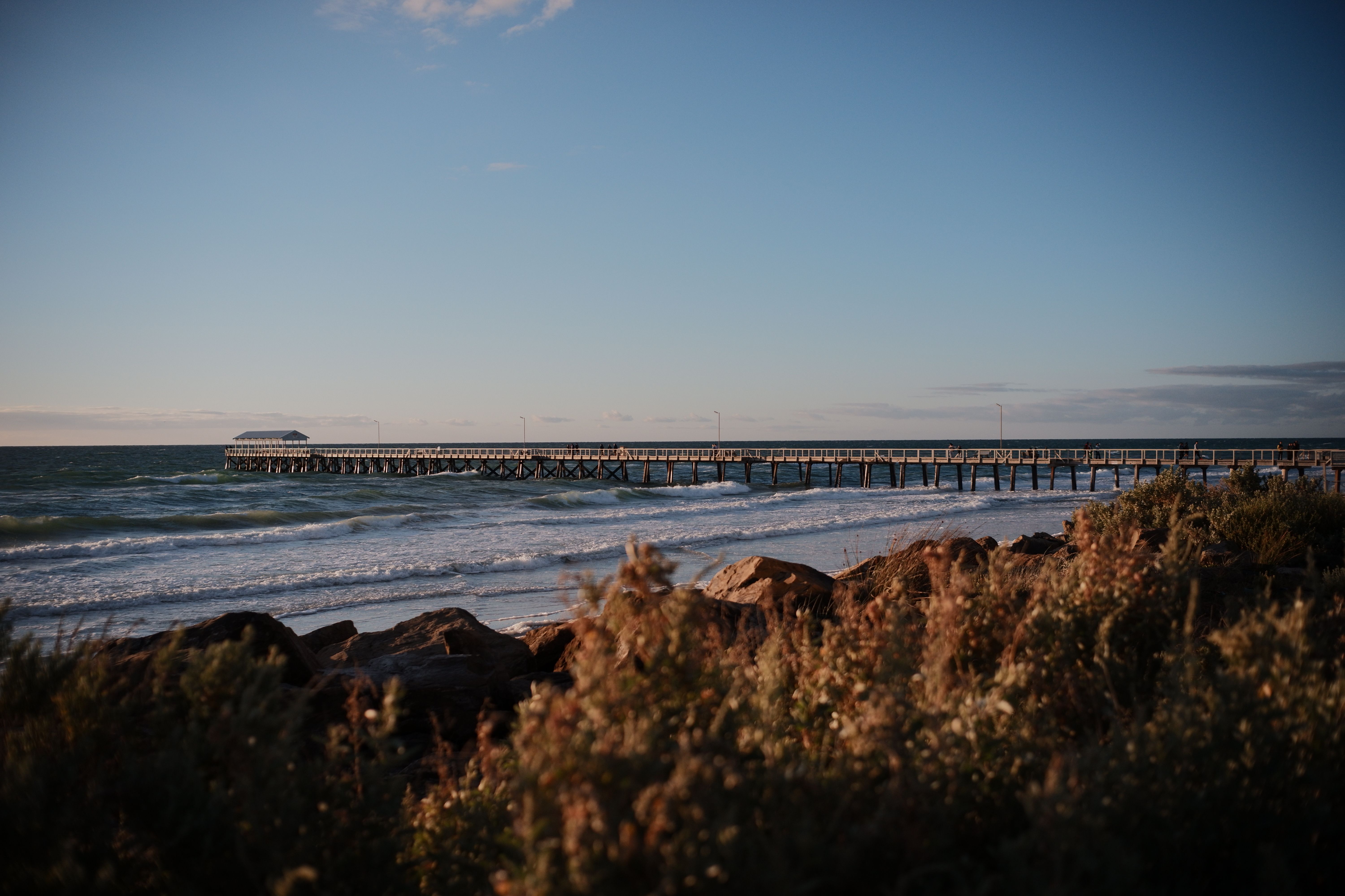 A stunning view of the coastline featuring a long pier extending into the sea during sunset.