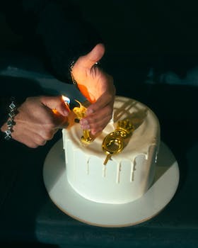 Close-up of hands lighting golden candles on a white cake, celebrating a birthday.