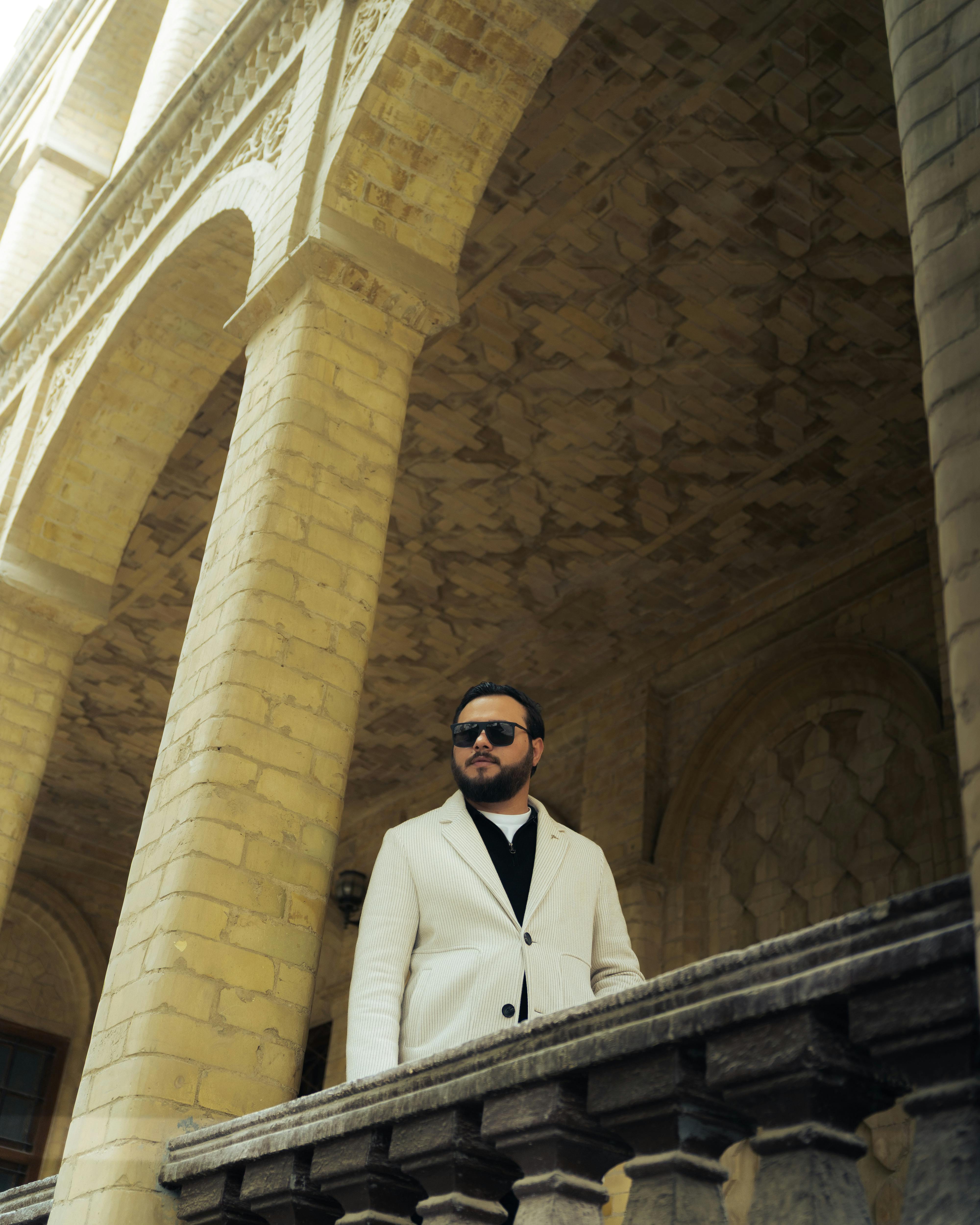 De franc Home elegant amb vestit blanc dret en un balcó històric amb arcs. Foto d'estoc