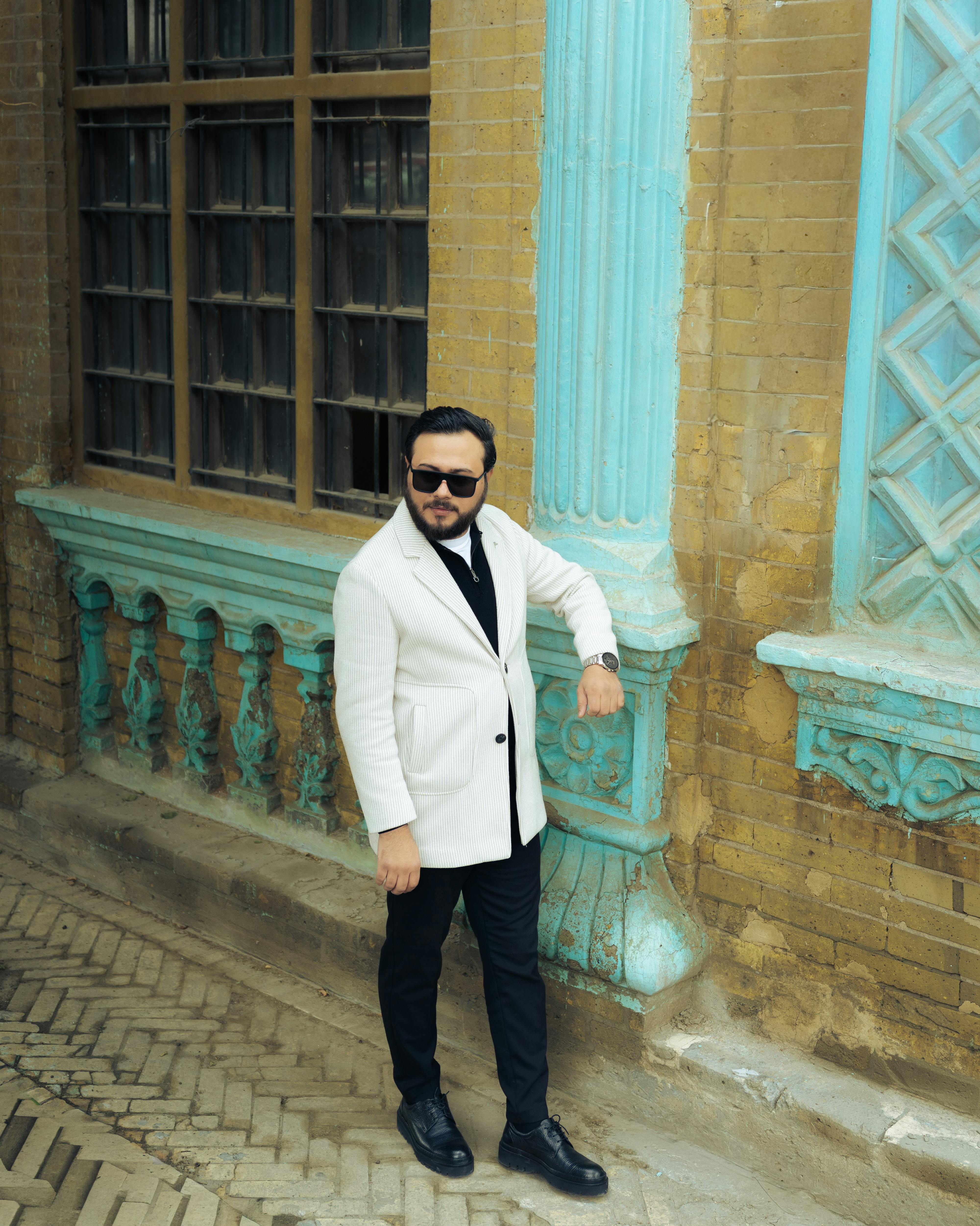 De franc Un home amb jaqueta blanca posa al costat d'un edifici històric ornamentat amb detalls blaus. Modern i elegant. Foto d'estoc