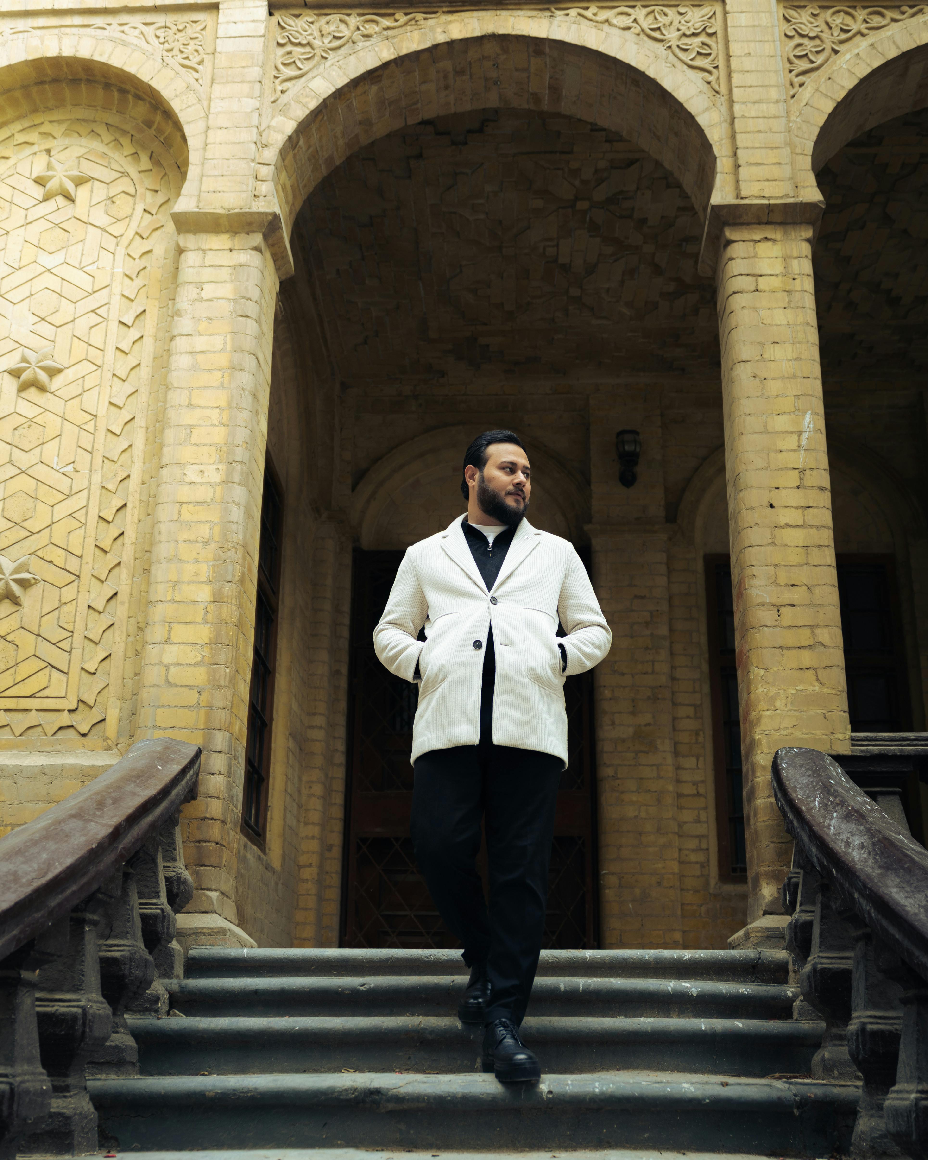 Man in white jacket descends historic stone staircase of an ornate building.