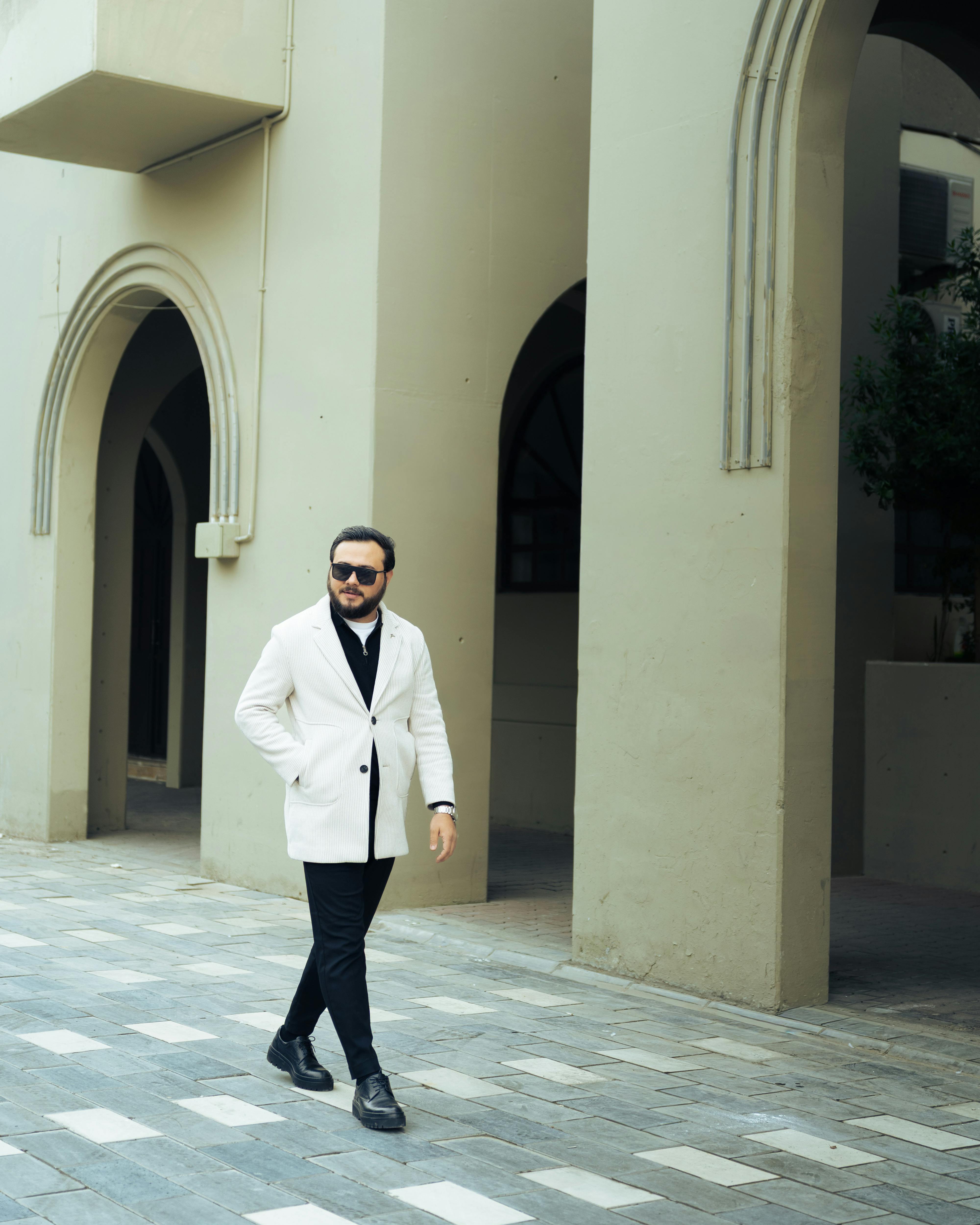 De franc Home segur amb jaqueta blanca caminant per una arquitectura contemporània amb arcs. Foto d'estoc