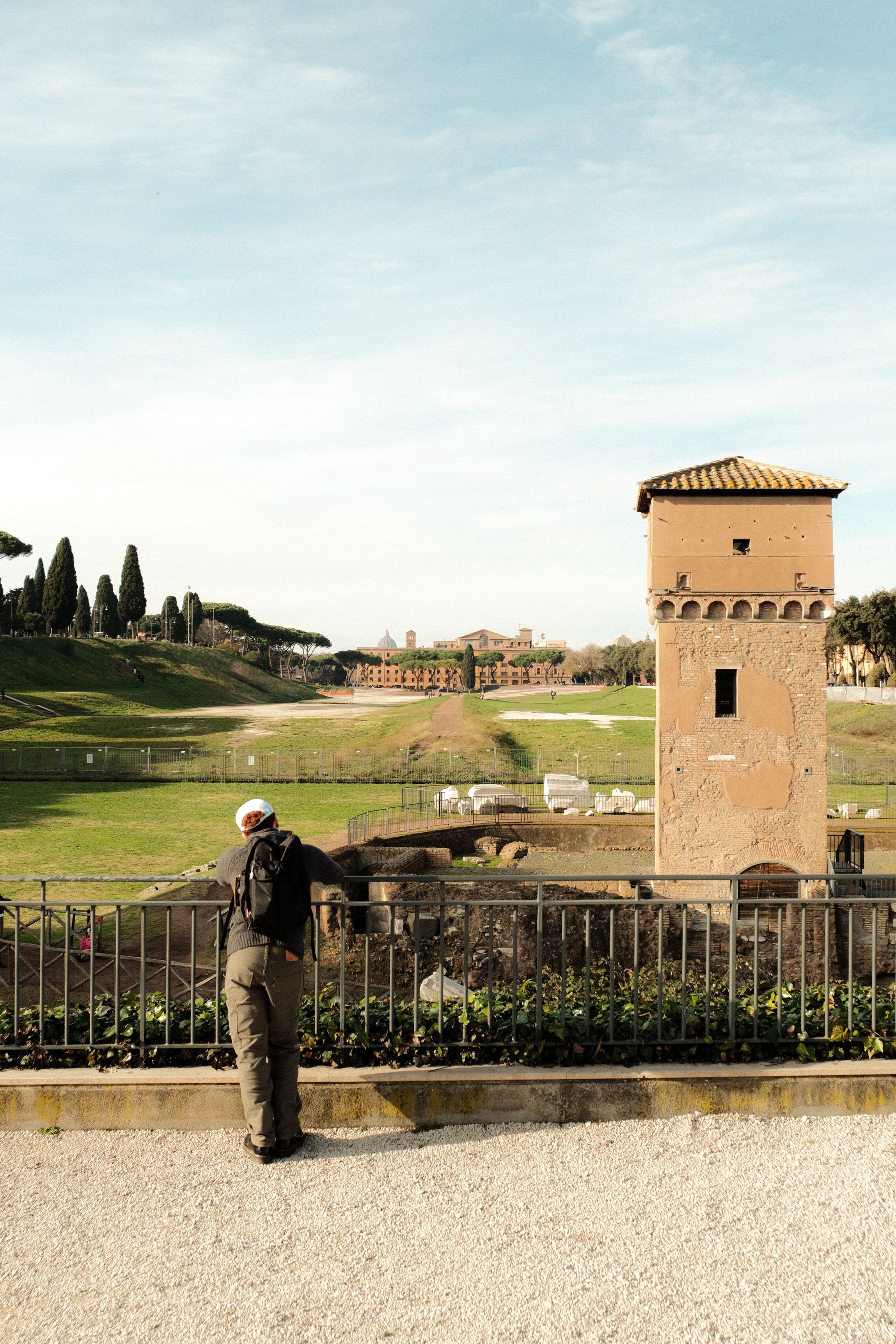 A person looks over a fence at historic Roman ruins during daylight.