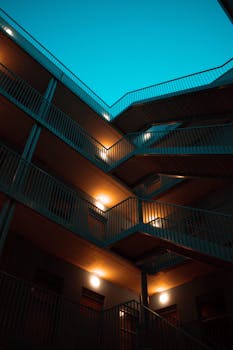 黄昏的天空下，一座现代化的多层建筑里，楼梯亮着灯光