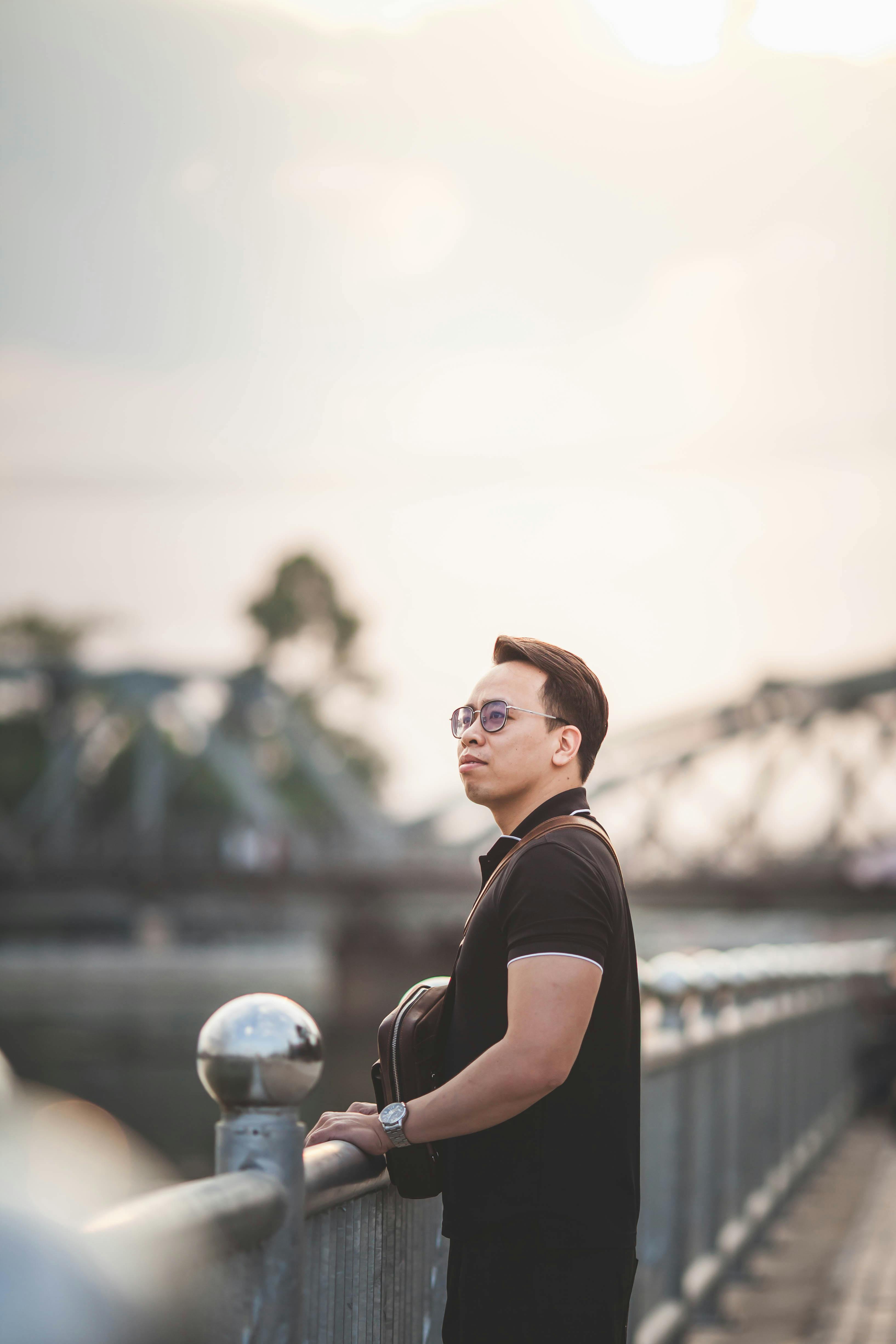 Gratuit Un homme se tient pensivement sur la rambarde d'un pont au coucher du soleil, créant une ambiance sereine et introspective. Photos