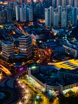 Aerial view of a bustling cityscape at night with illuminated skyscrapers and vibrant street lights.