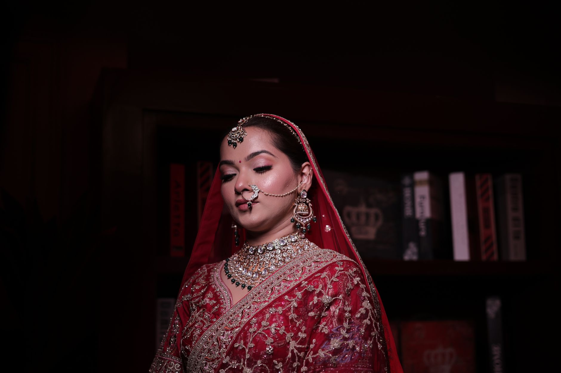 Elegant Indian bride in red sari with intricate jewelry, posing indoors.