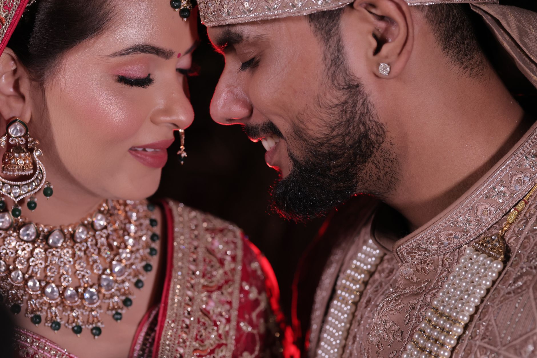 Close-up portrait of a joyful Indian couple in traditional wedding attire, showcasing intricate jewelry and embroidery.
