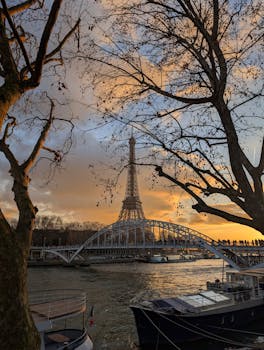 Eiffel Tower framed by trees during a vibrant sunset over the Seine river in Paris.
