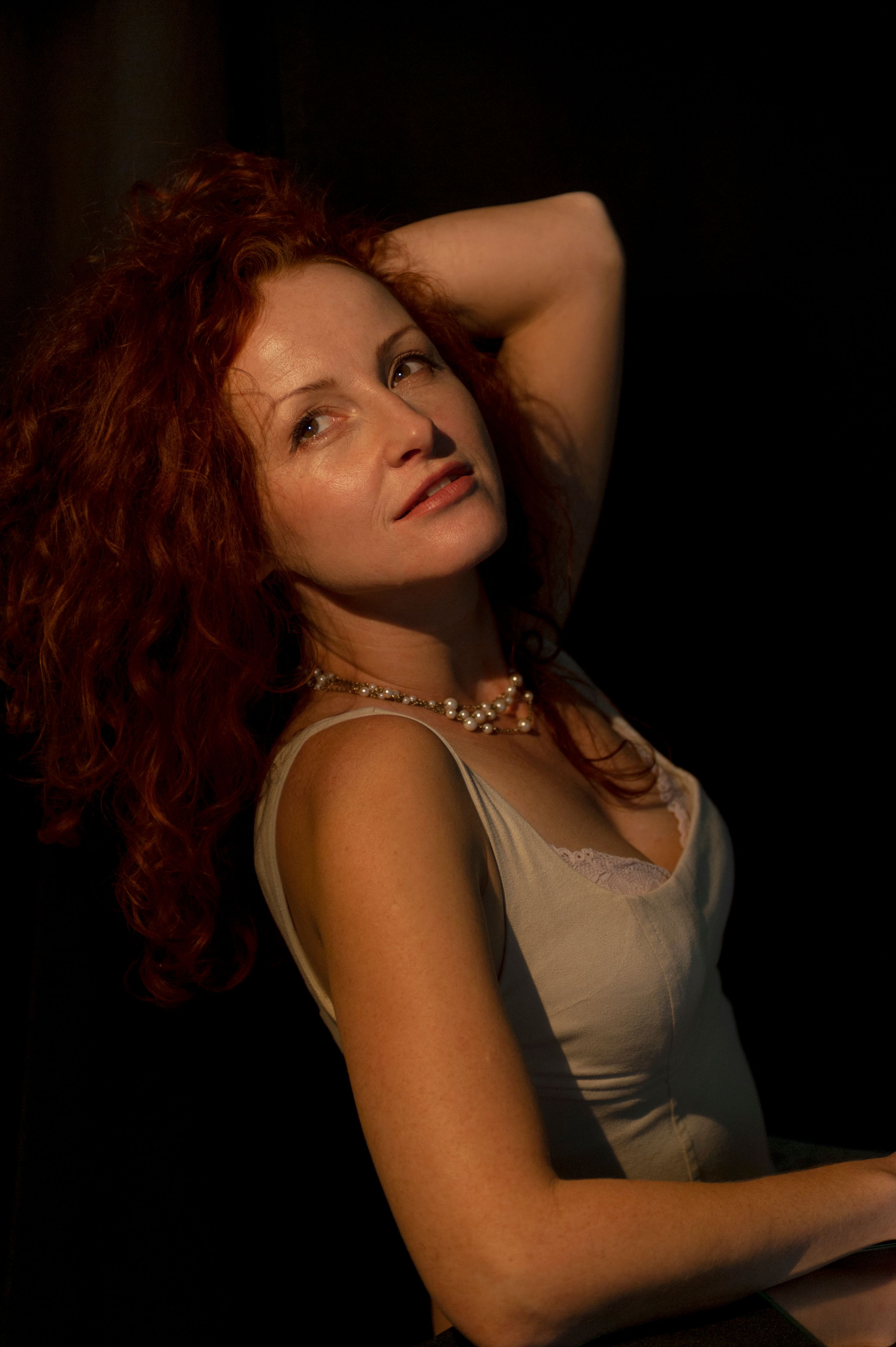 Portrait of a red-haired woman in elegant pose and dramatic lighting, highlighting her natural beauty.