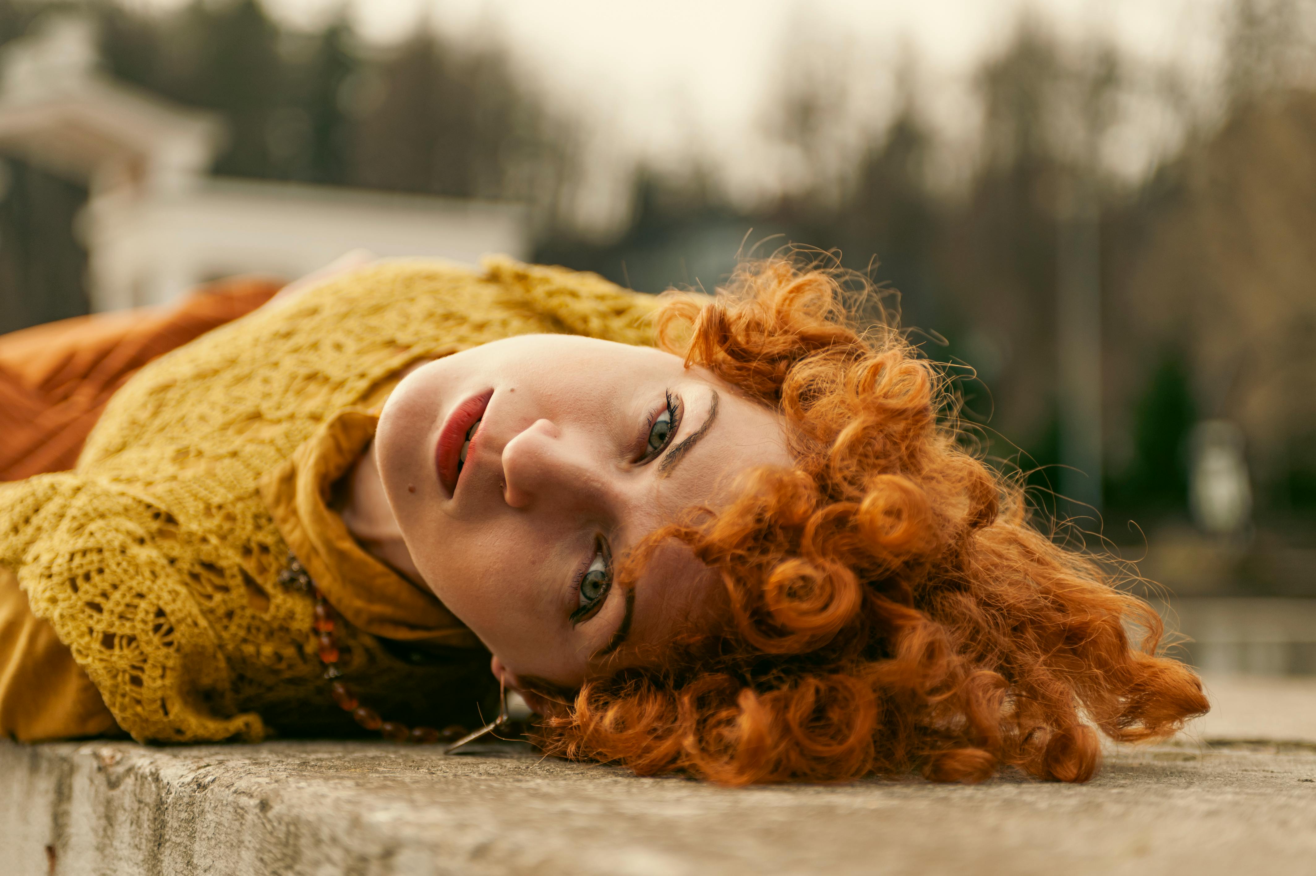 De franc Retrat artístic d'una dona amb els cabells arrissats vermells estirada sobre una superfície de pedra a l'óblast de Lviv, Ucraïna. Foto d'estoc