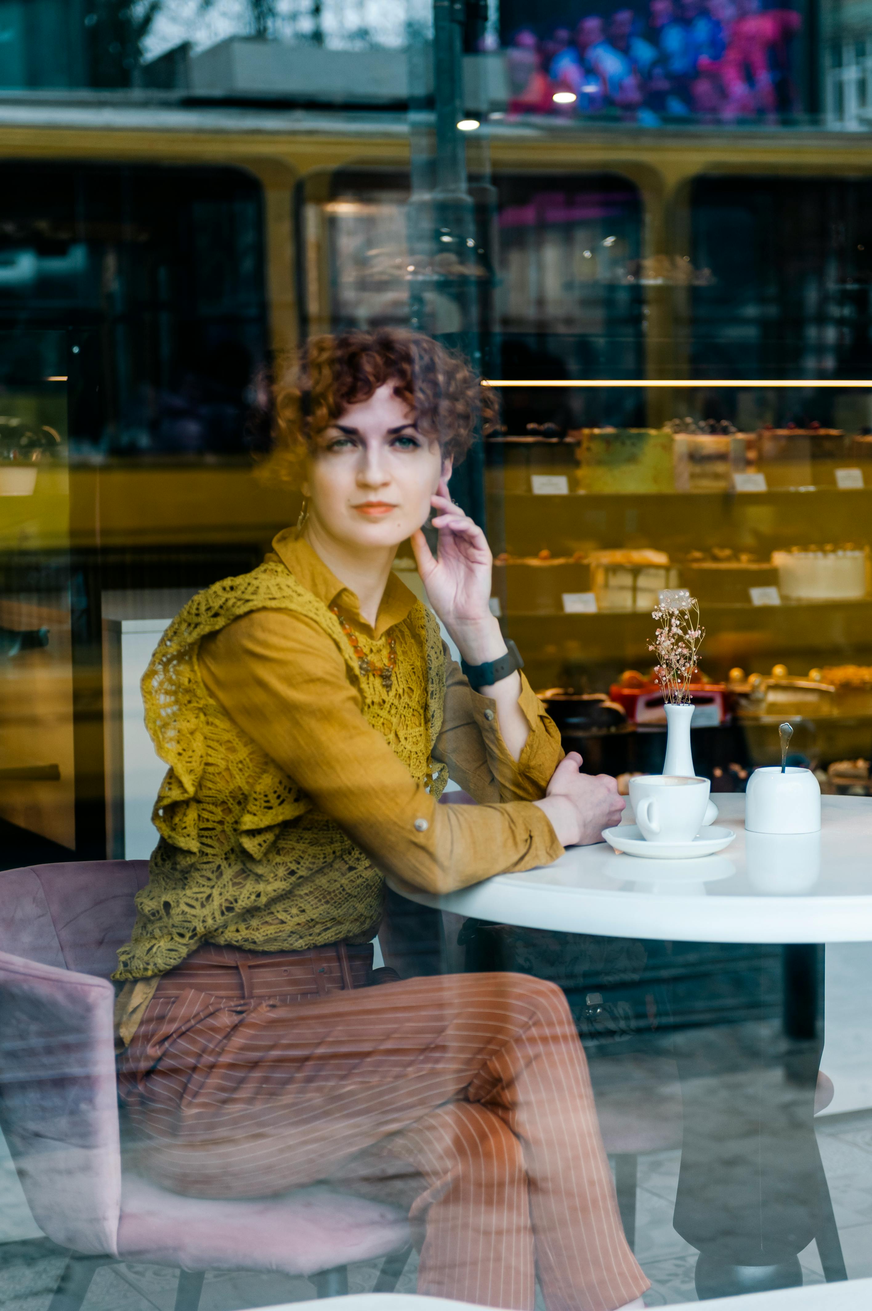 Gratis Mujer sentada dentro de un acogedor café en una ciudad europea, reflejando la vida urbana exterior. Foto de stock