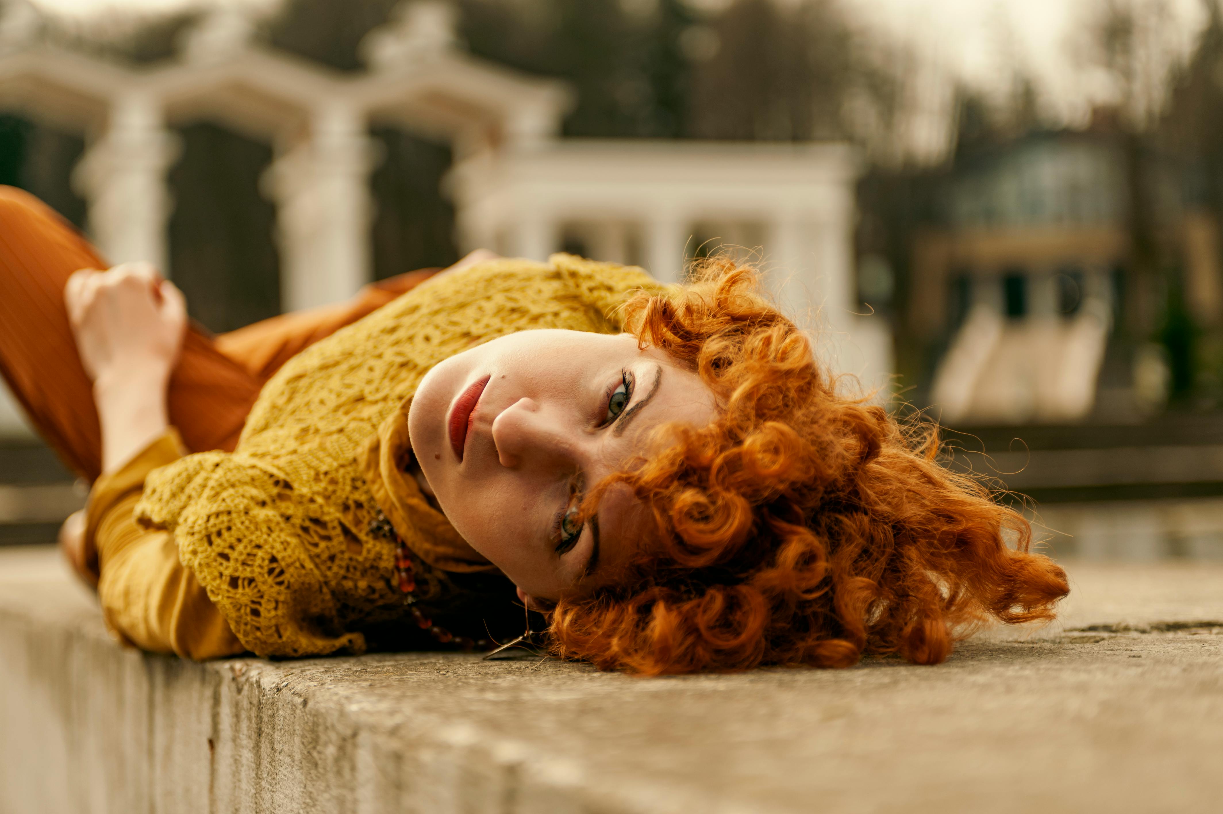 Kostenlos Porträt einer rothaarigen Frau, die in einem Stadtpark in Lwiw, Ukraine, auf einer Steinstruktur liegt. Stock-Foto