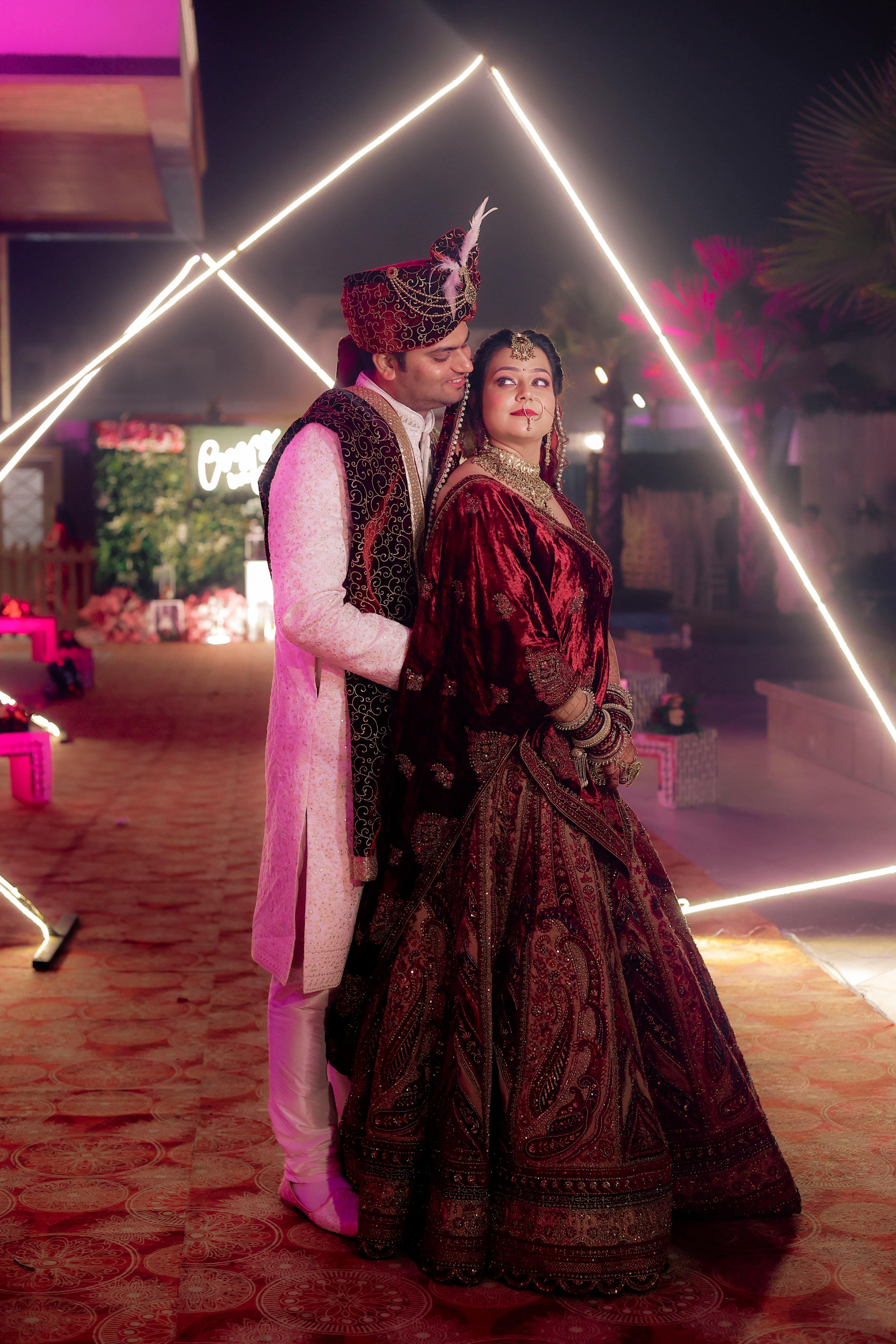 De franc Una parella amb vestit tradicional de casament indi posa sota una il·luminació geomètrica. Foto d'estoc