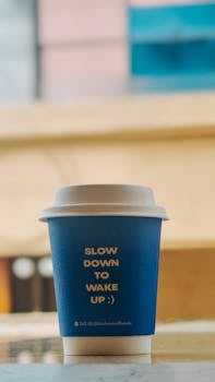Blue coffee cup with text 'Slow Down to Wake Up :)', on a table.