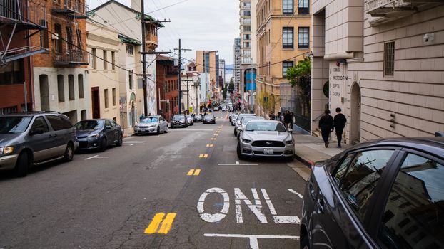 Busy urban street scene with cars parked along a hilly road in San Francisco, featuring typical architecture.