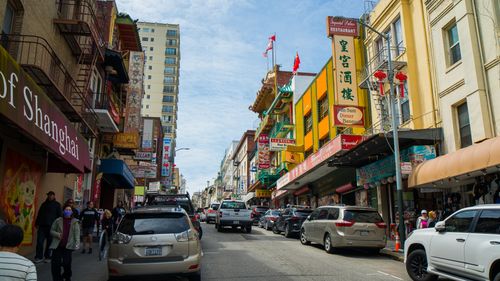 Free Vibrant street scene in Chinatown, San Francisco with shops, people, and cars under a clear sky. Stock Photo