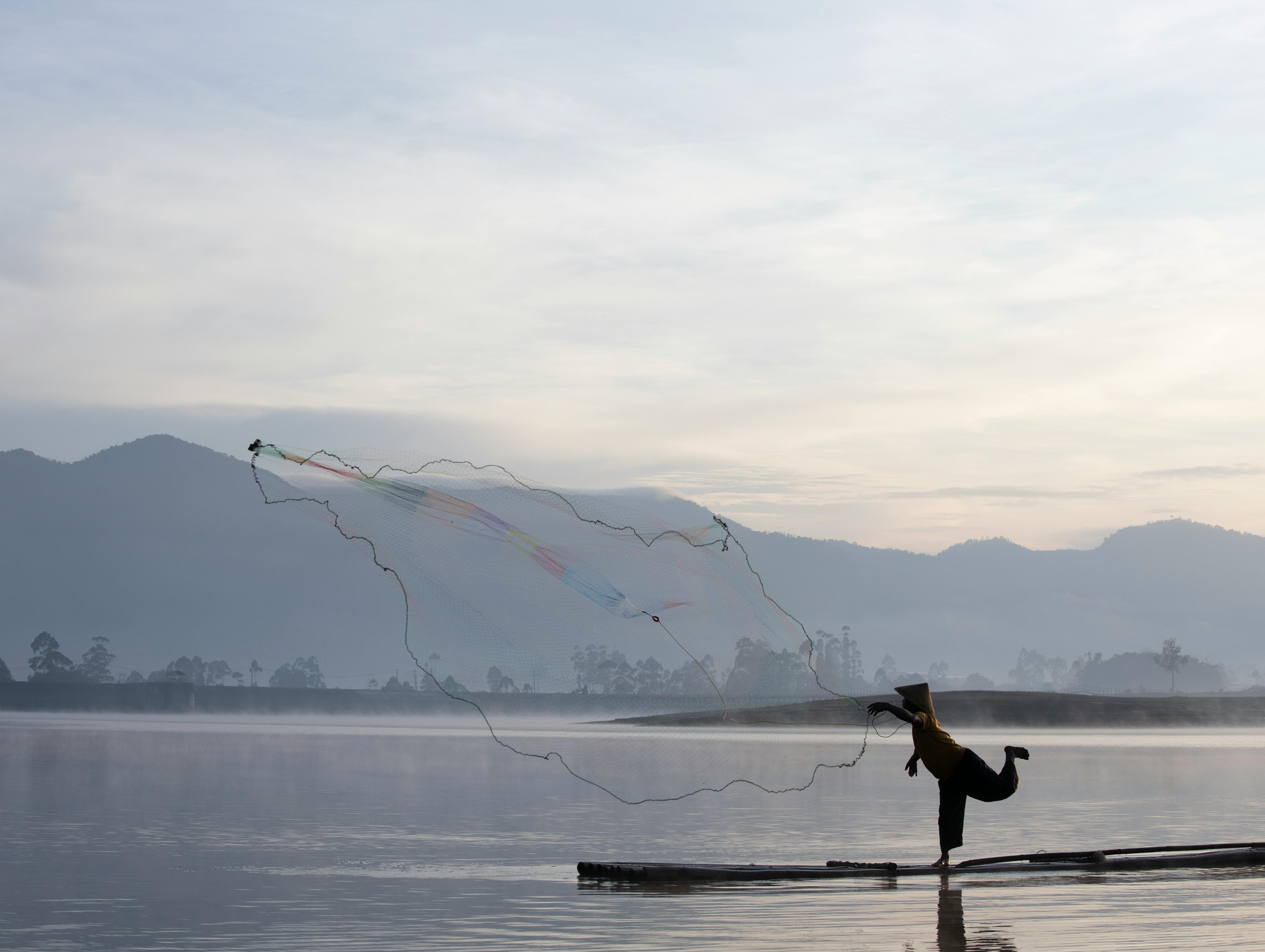 Gratuit Silhouette d'un pêcheur jetant habilement un filet à l'aube sur le serein lac Situ Cileunca, à Java Ouest, en Indonésie. Photos