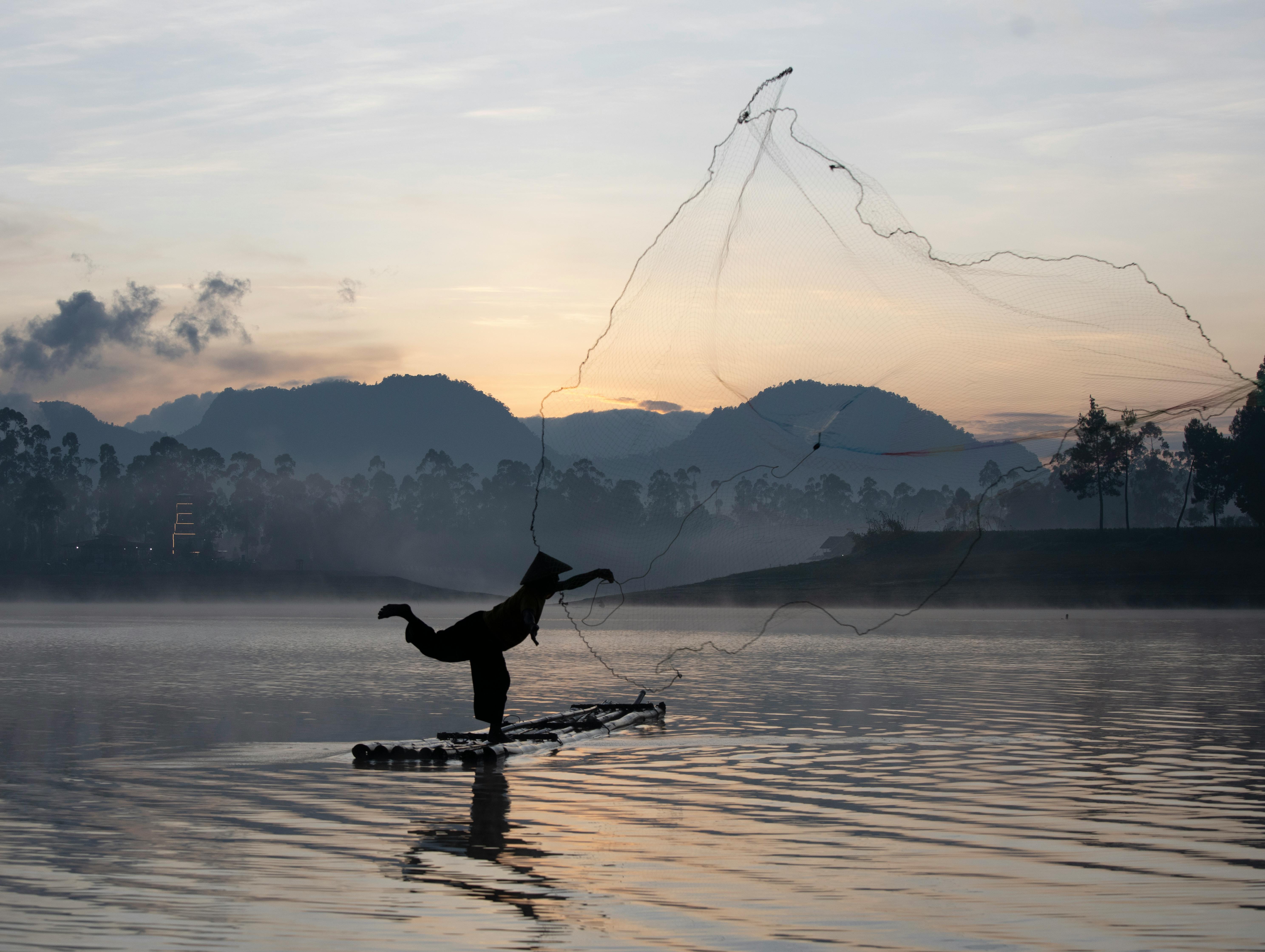 Gratuit Scène sereine d'un pêcheur jetant son filet au lever du soleil sur le lac Situ Cileunca, à Java Ouest, en Indonésie. Photos