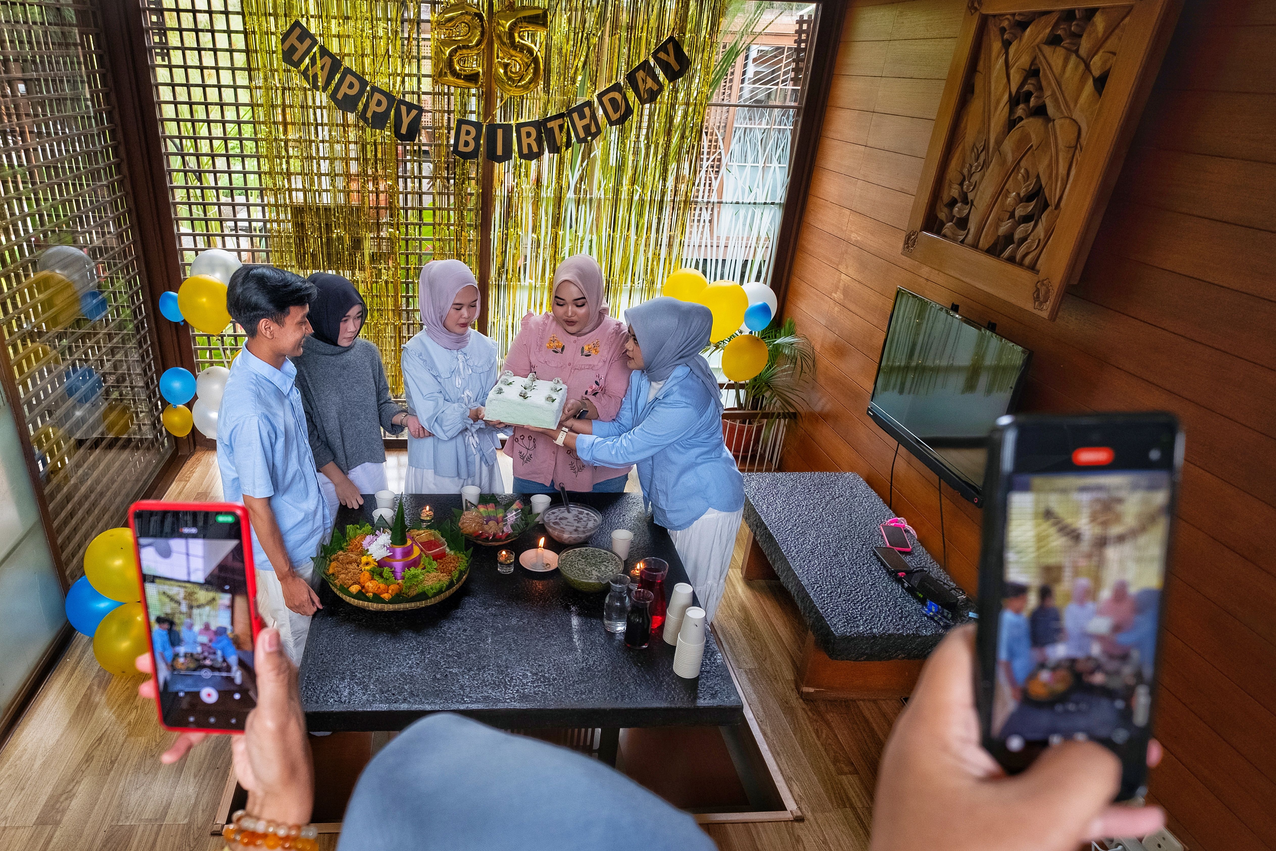 Group celebrating with cake and balloons indoors.