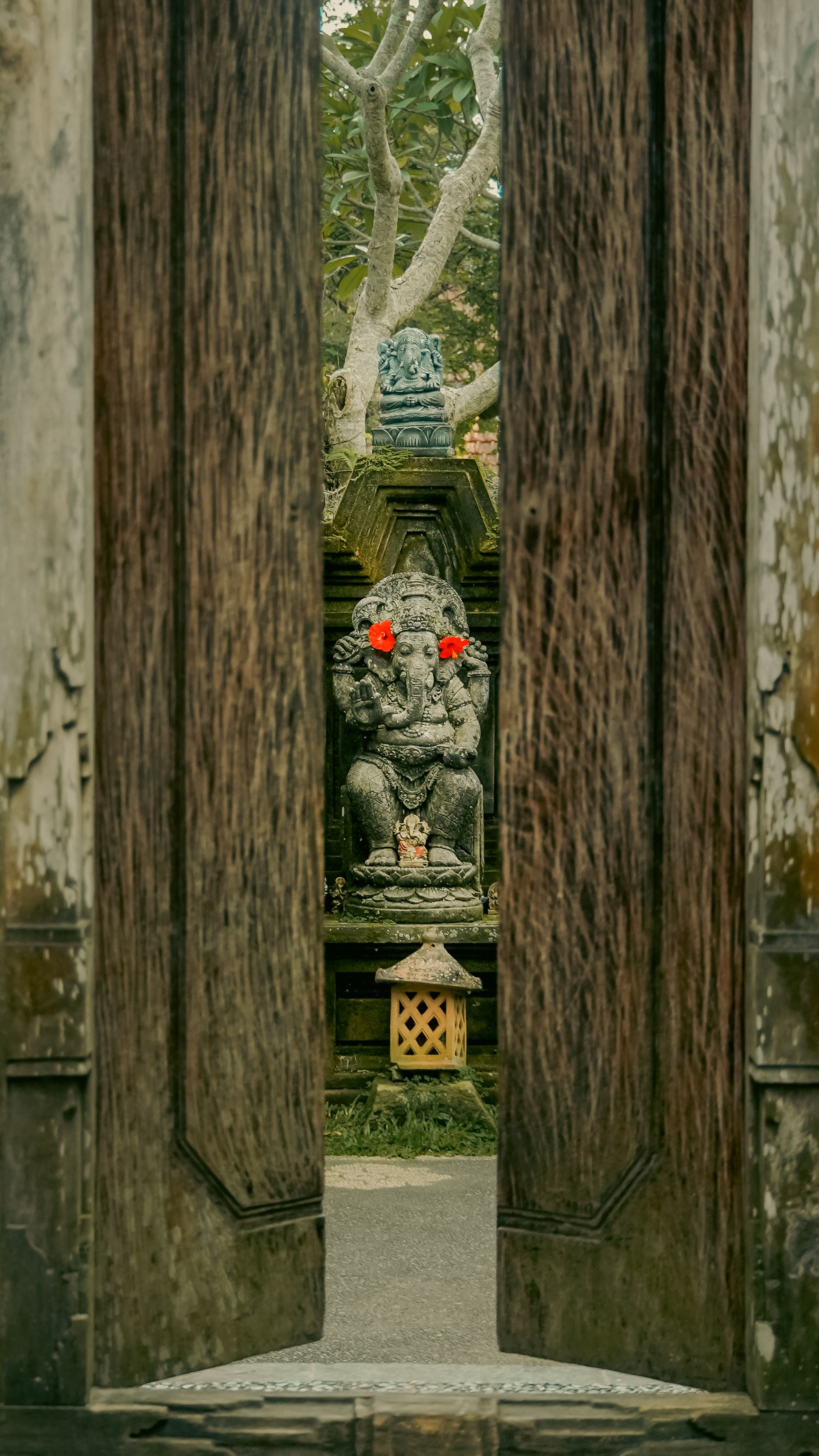 A sacred Ganesha statue with red flowers viewed through wooden temple doors, rich cultural essence.