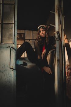 Chic woman posing indoors with stylish attire, creating a moody urban atmosphere.