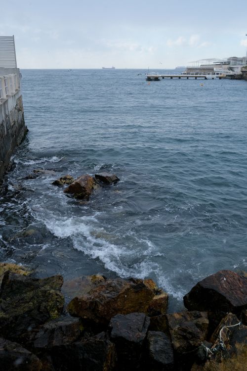 Free Dramatic rocky shoreline with waves and distant pier under cloudy skies. Stock Photo