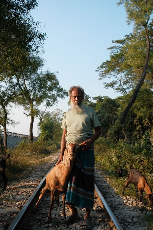 Free Portrait of an elderly man with a goat on a tranquil railway track in a rural setting. Stock Photo