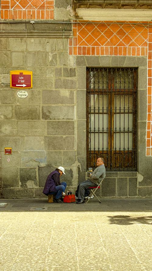 Free Locals interacting on a street in Puebla with a historic architecture backdrop, showcasing daily life. Stock Photo