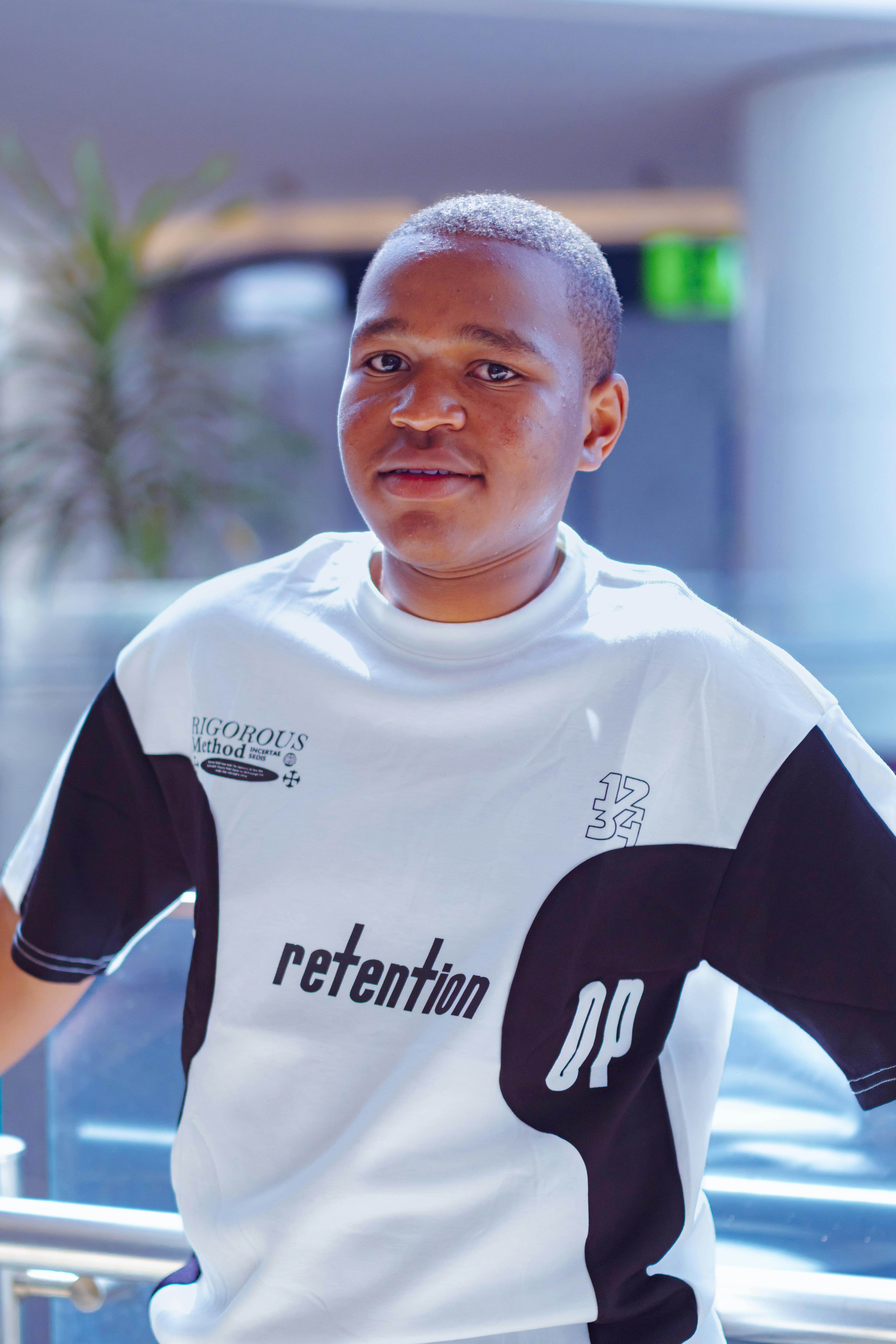 A young man poses casually indoors wearing a stylish black and white shirt.